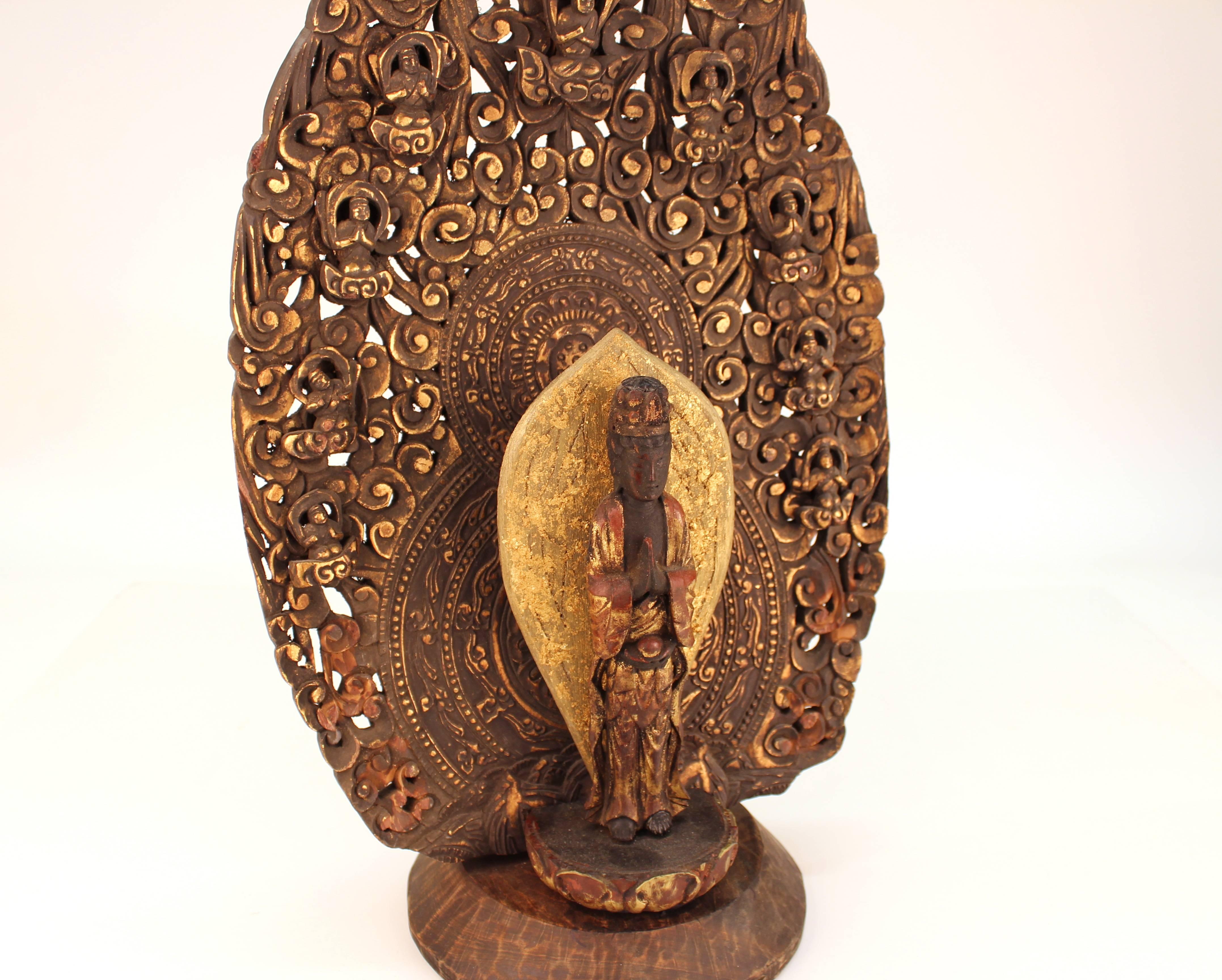 An Japanese Buddha sculpture in polychrome wood. The Buddha stands in Anjali Mudra, in a double mandorla; the first one leaf-shaped, the second one in stylized flames, studded with disciples.
In good vintage condition with a small hairline crack to