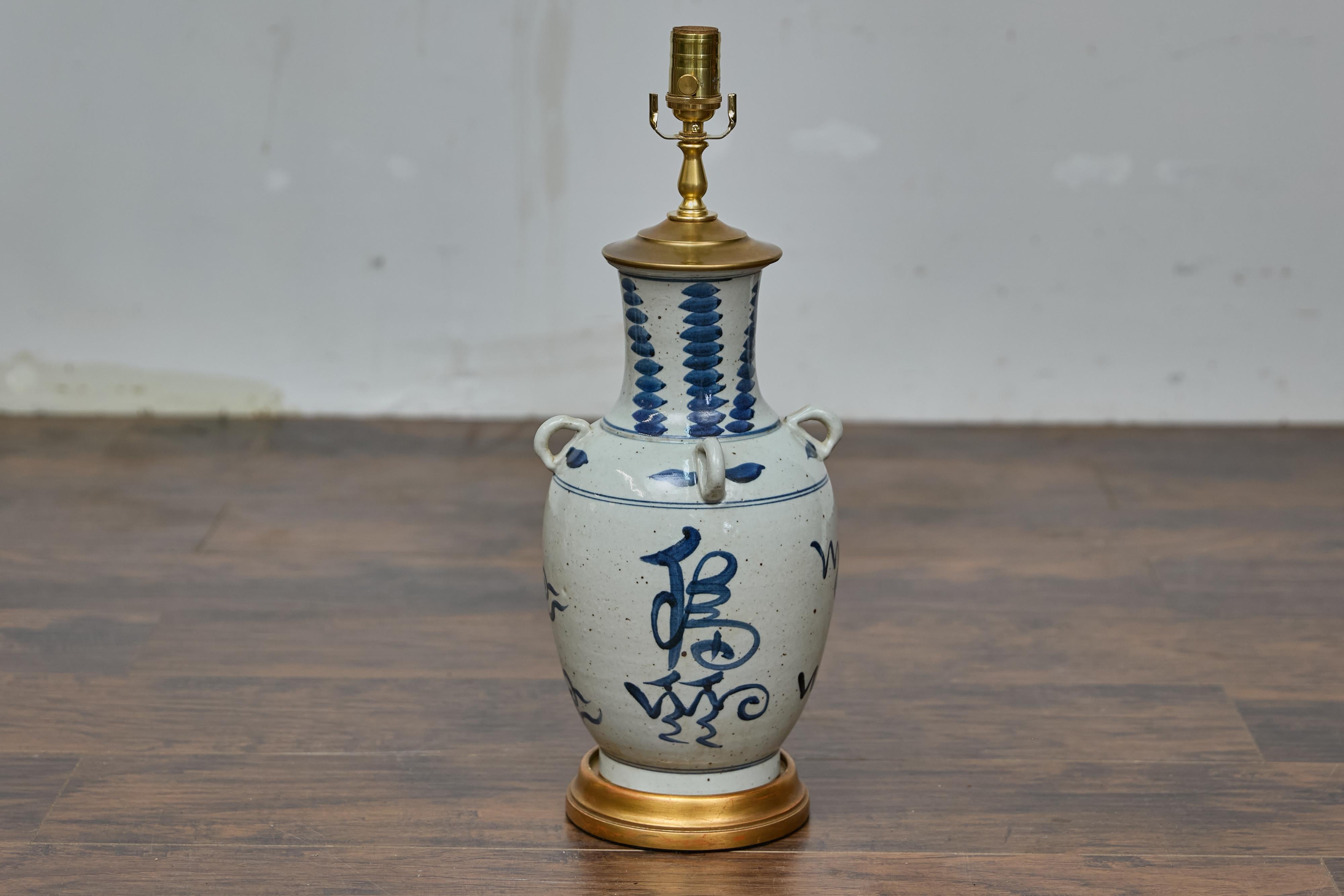 Asiatische Porzellan-Tischlampe mit vergoldetem Holzsockel, verkabelt für die USA. Diese auffällige Tischleuchte, die aus einem asiatischen Porzellangefäß gefertigt ist, strahlt zeitlose Eleganz aus. Mit handgemalten kobaltblauen Pinselstrichen,