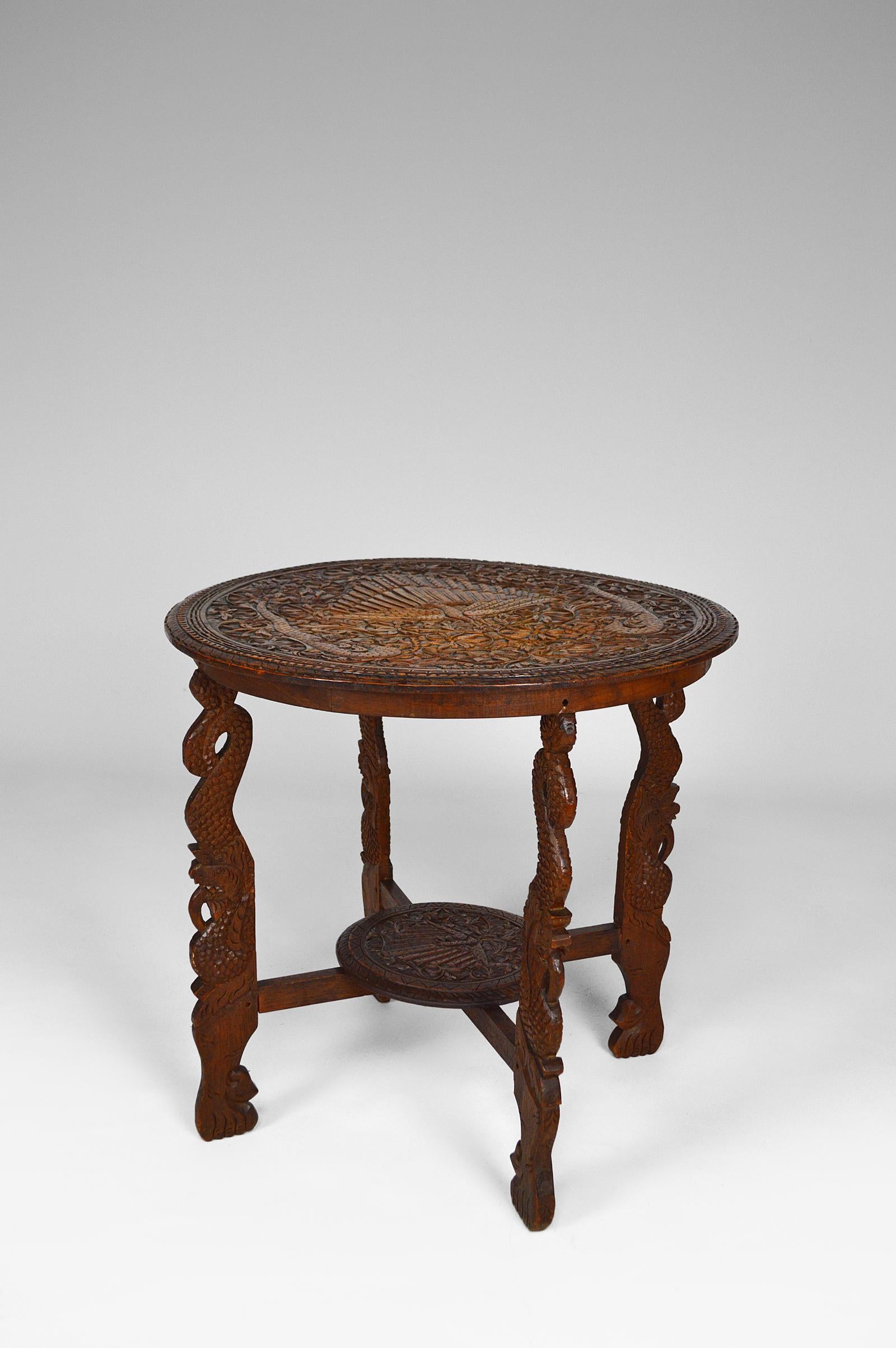 Superb Asian side table / tea or coffee table in carved solid wood.

The carved top represents a majestic peacock surrounded by two serpents or mythological dragons, resting around lush vegetation.
The feet are also carved in the shape of