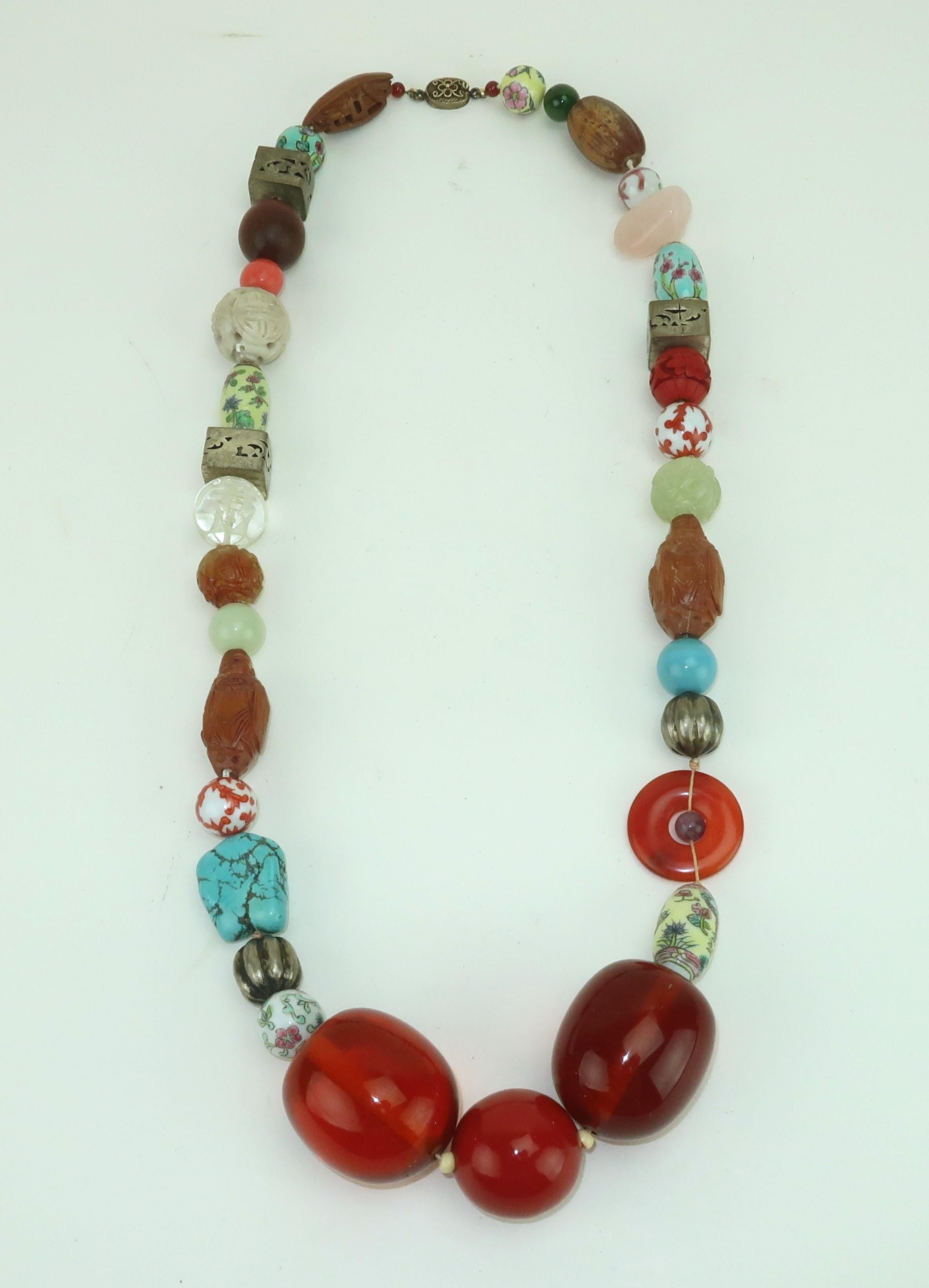 Vintage Asian beaded necklace designed with a colorful mix of semi-precious stones, carved wood Buddhas, Chinese silver, ceramics, cinnabar and resin with the appearance of amber.  The beads are strung onto a knotted cord and outfitted with a