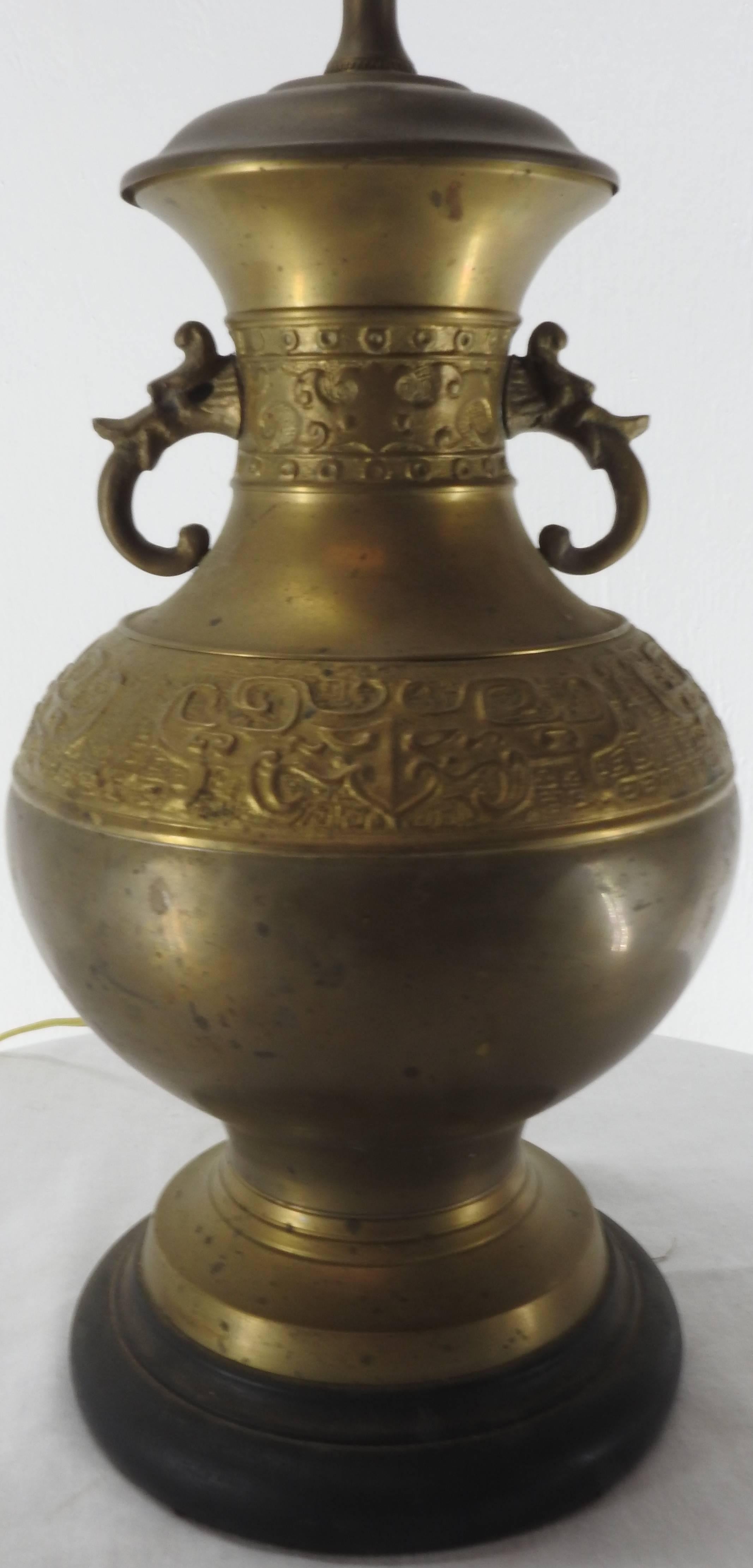 We are offering a cast brass lamp with elegantly scrolled arms and detailed embossing. The lamp sits atop a black base. You will receive the harp to attach your shade and it is topped off with an oriental finial. The embossing adds a distinct air of