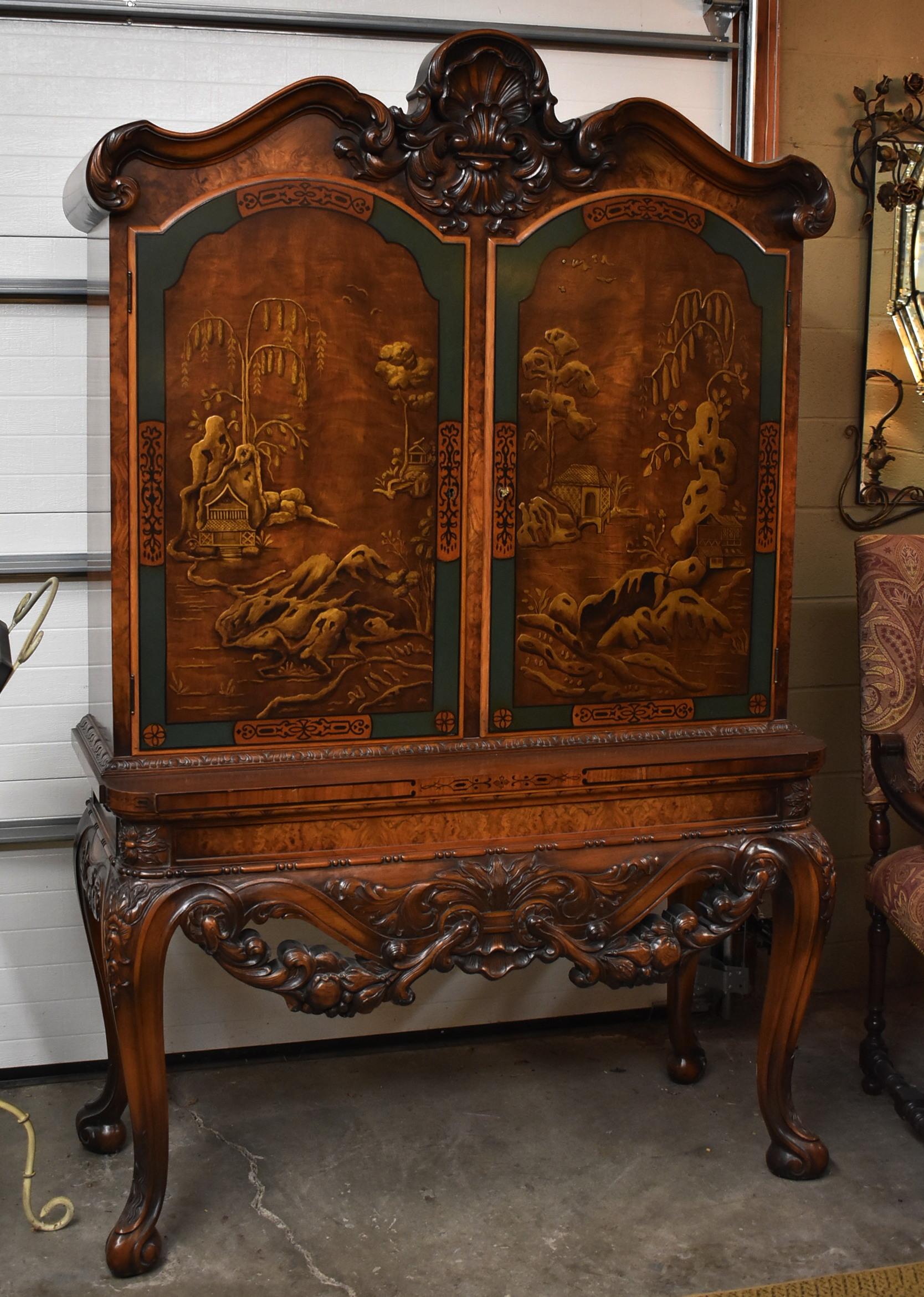 Asian style locking bookcase / cabinet with low relief carved landscape and houses. Made of walnut and burlwood, heavily carved apron of swagged fruit and shell detail at the top, with hand painted doors. Two interior adjustable shelves. Very solid,