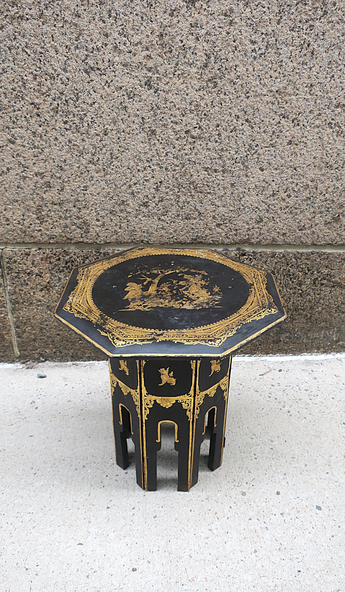 An octagonal tabouret side or drinks table with black and gold applique, circa early-20th century, Asia, likely Burma. Tables' octagonal top and base are attached. Gold decoration on top surface (garden scene) and around base (foo dogs and boarder