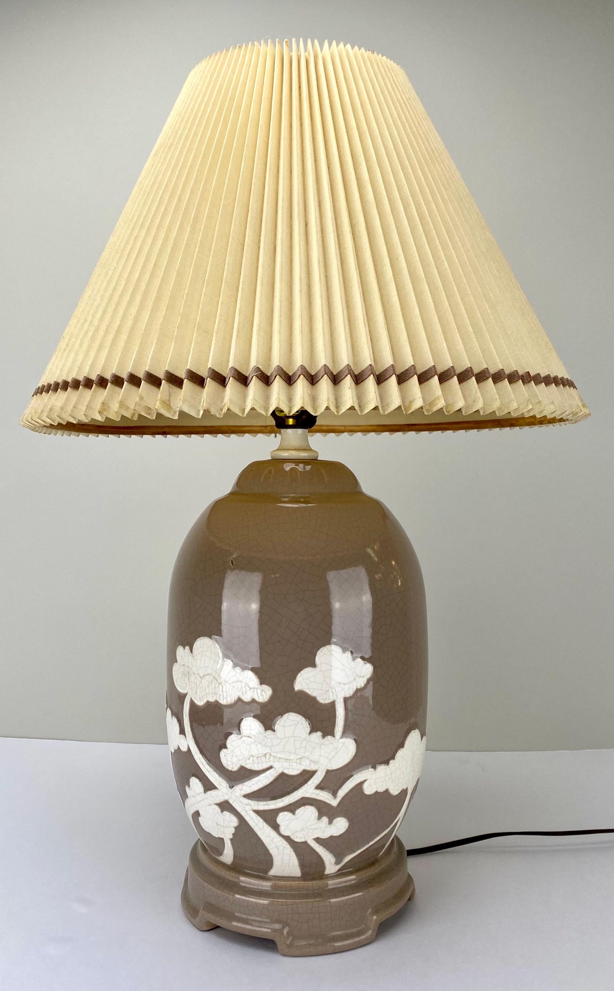 A pair of Asian Mid-century round ceramic table lamps, each exuding a timeless elegance through their stylish taupe color. The lamp bodies are adorned with a delicate white relief design, depicting the graceful silhouette of bonsai trees, adding an