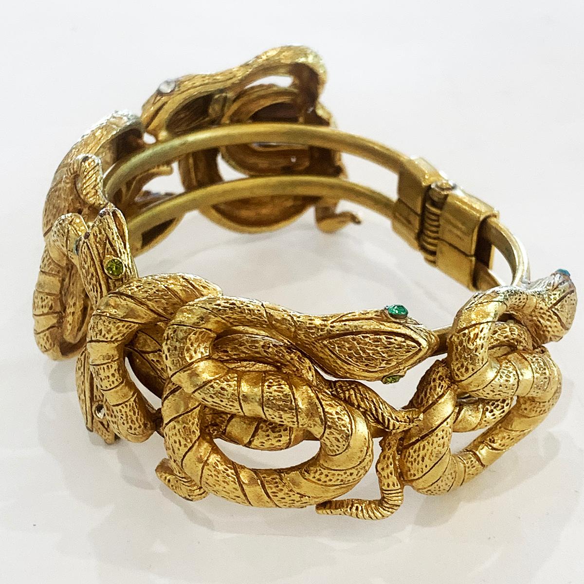 An Egyptian Revival Snake Clamper Bangle by Askew of London, with highlights of mixed Diamantes to eyes. Comprising the rich 24ct Gold finish with 6 snakes intertwined, 3 each side of the Bangle opening. The gold finish is excellent with great, rich