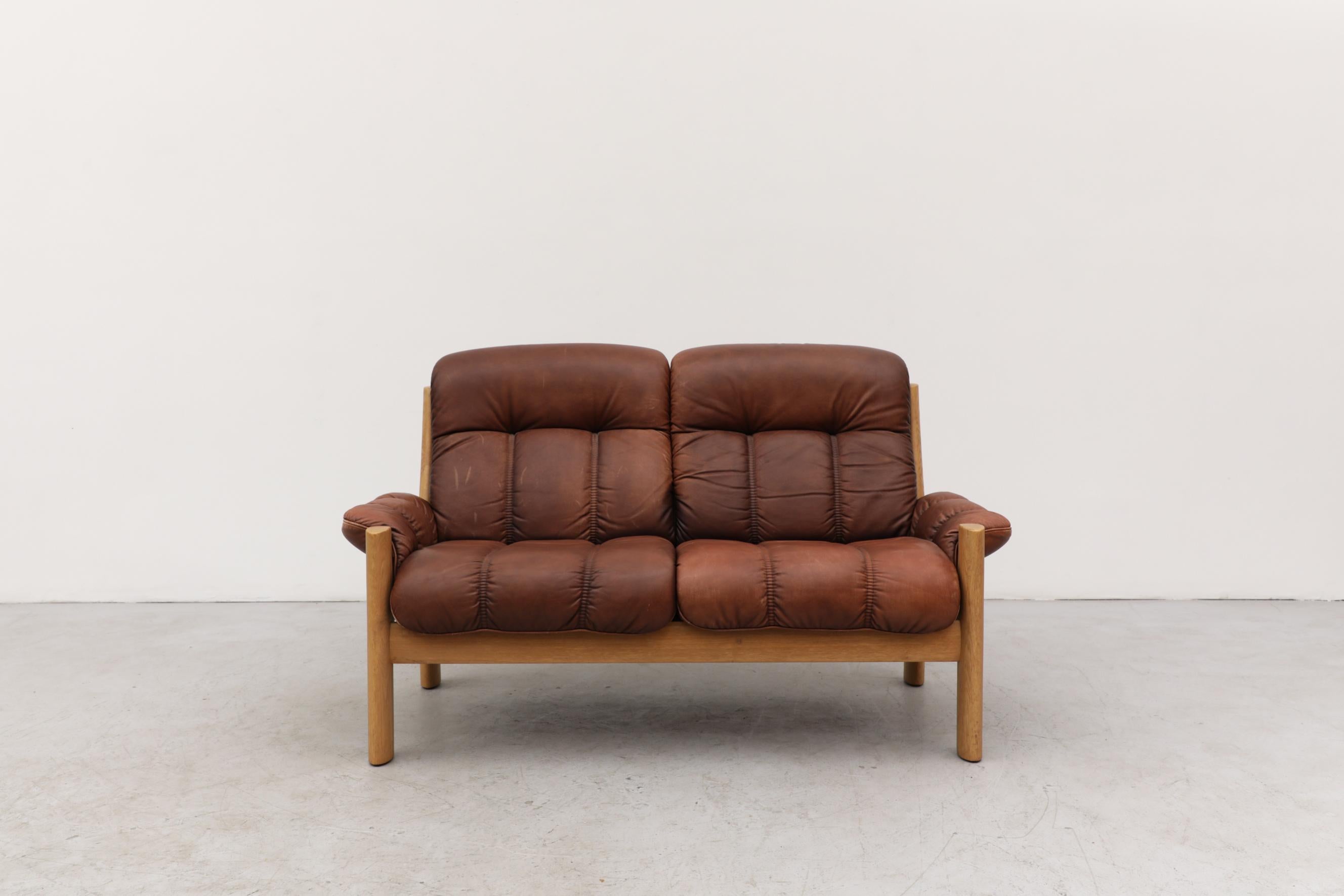Tufted leather and oak loveseat with a visible patina by Finnish design company, Asko. The leather is in original condition and has some scratching and wear that is consistent with its age and use. An Asko lounge chair, sofa