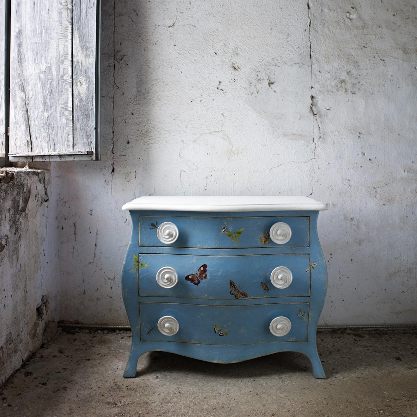 Introducing the Asolo chest in Parma blue, a hand-painted masterpiece adorned with charming butterfly motifs. Its elegant curves and soothing color create a warm and inviting ambiance. Customizable in size and design. Please, ask the Concierge