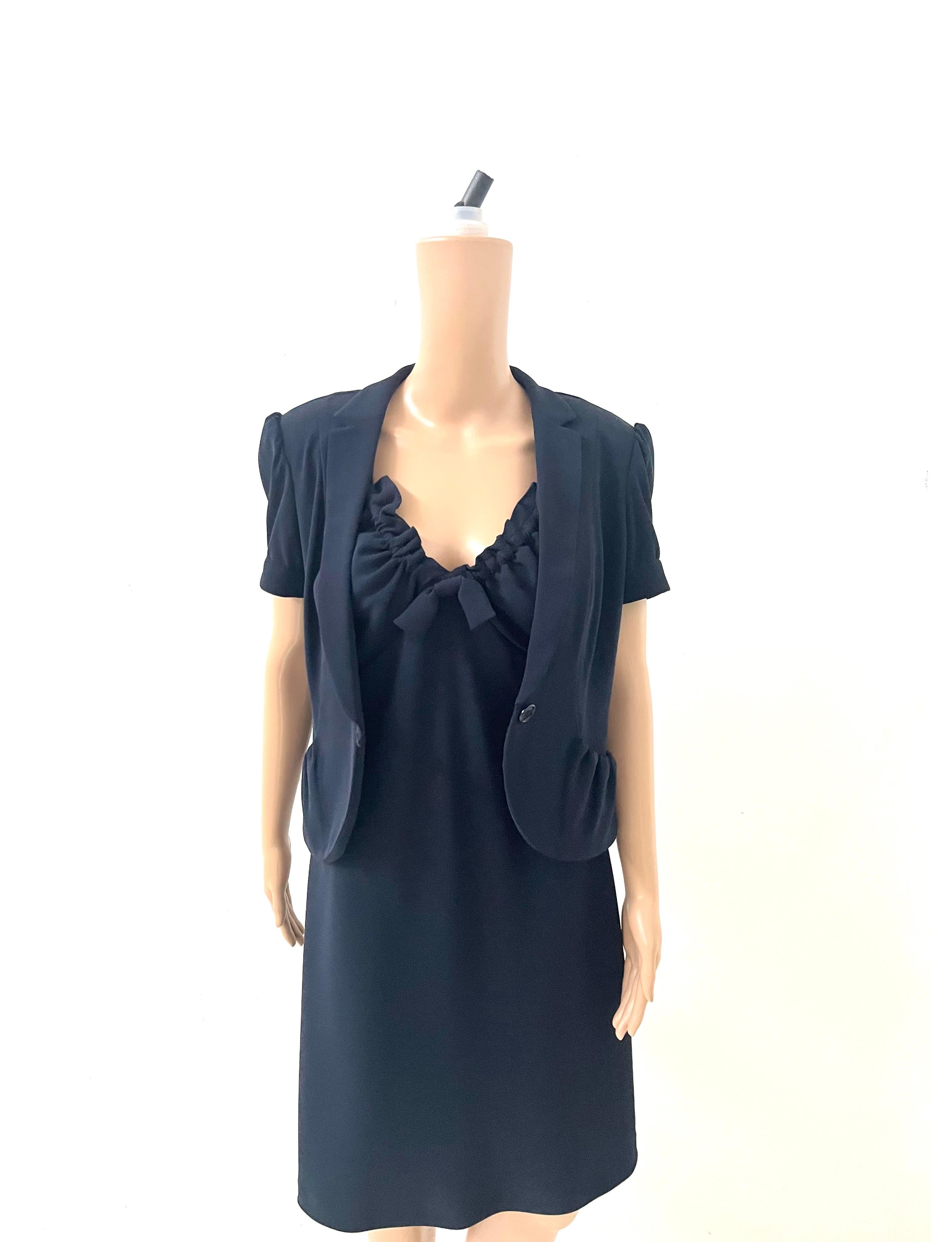 This elegant two-piece set by Aspesi is a rare vintage find from the early 2000s, made in Italy and crafted with the brand's signature understated refinement. It includes a sleeveless black dress with ruched neckline and bow detail, paired with a