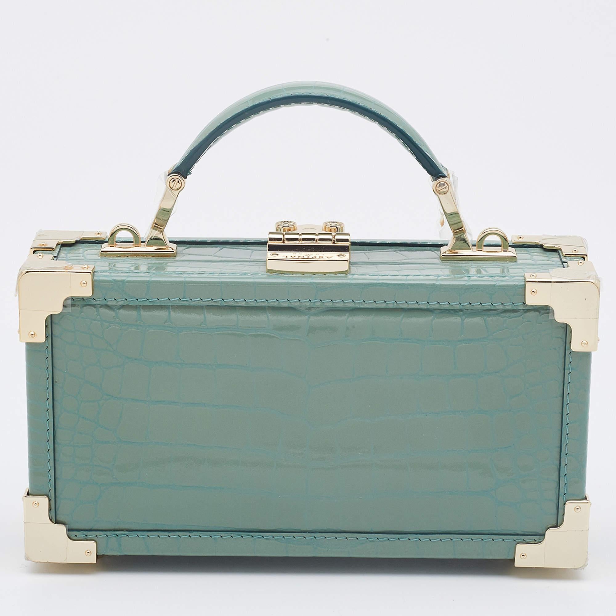 Crafted from croc-embossed patent leather in a lovely green hue, this Trinket bag is just amazing! Aspinal Of London has designed this luxurious top handle bag with a spacious fabric interior. It has an exquisite design, a detachable chain link, and