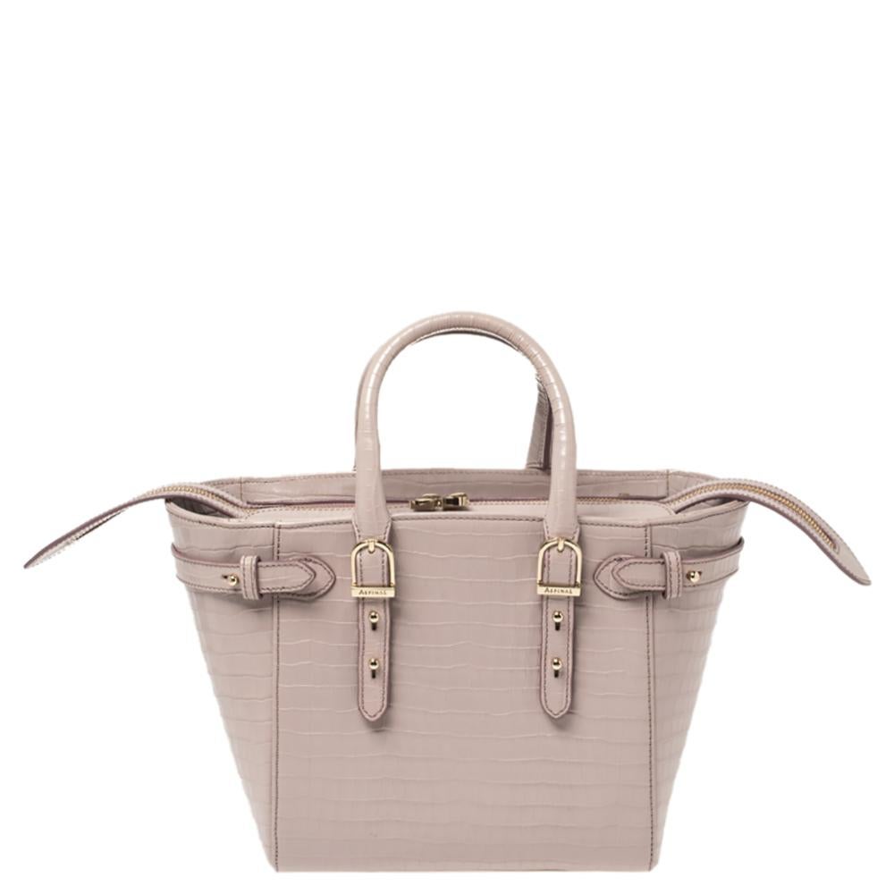Designed for busy, on-the-go women, this Marylebone tote from Aspinal of London is a melange of style and practicality. Crafted in lilac croc-embossed leather, it features dual top handles, buckle detailing on the top edges, and metal feet at the