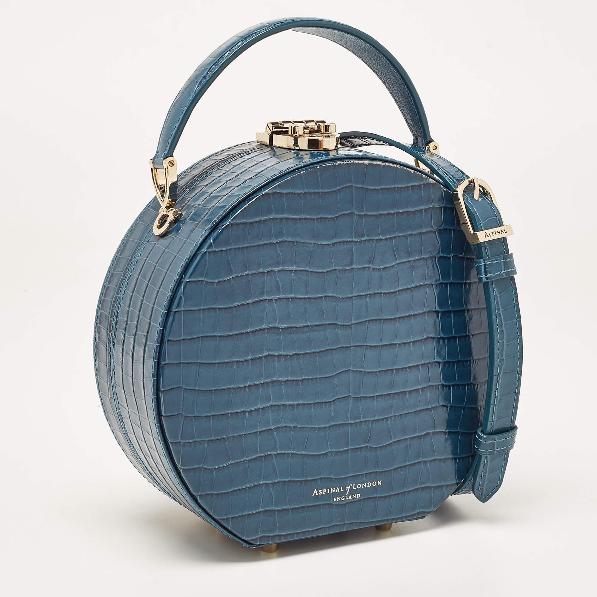 This petite and luxurious bag from Aspinal of London is crafted from croc-embossed teal blue leather, offers a top handle, and comes with an optional shoulder strap. It has a canvas-lined interior to accommodate your essentials and gold-tone studs