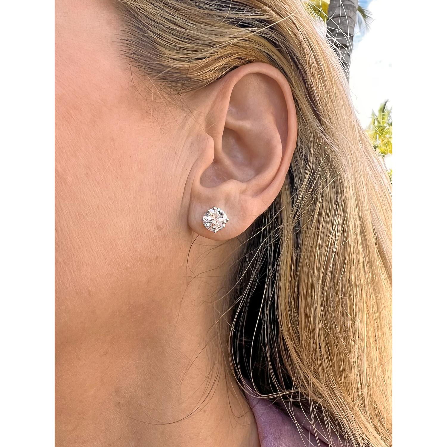 Round brilliant-cut diamond stud earrings, showcasing a pair of well-matched near-colorless diamonds weighing 3.03 total carats, the diamonds secured in four-prong 18k white gold settings with posts and friction backs for pierced ears. Both diamonds