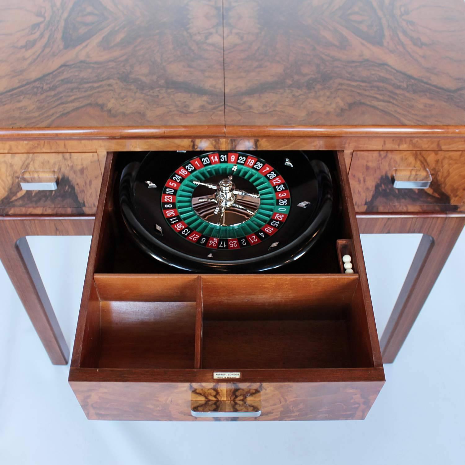 An Art Deco gaming table by Asprey of London.

Figured walnut throughout with straight grain walnut banding. Opens over integral, baize covered slides to full gaming table. Includes original chemin de for and gaming chips. Later roulette wheel.