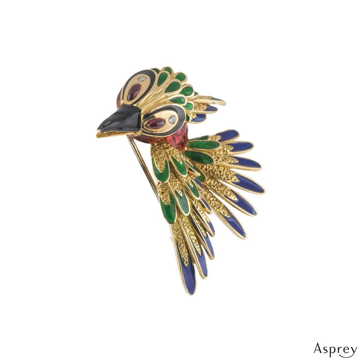 A unique 18k yellow gold Asrey woodpecker brooch. The brooch comprises of a flying woodpecker motif with blue, green, black and red enamel. The eyes have a cabochon cut ruby and round brilliant cut diamonds. The rubies have a total approximate