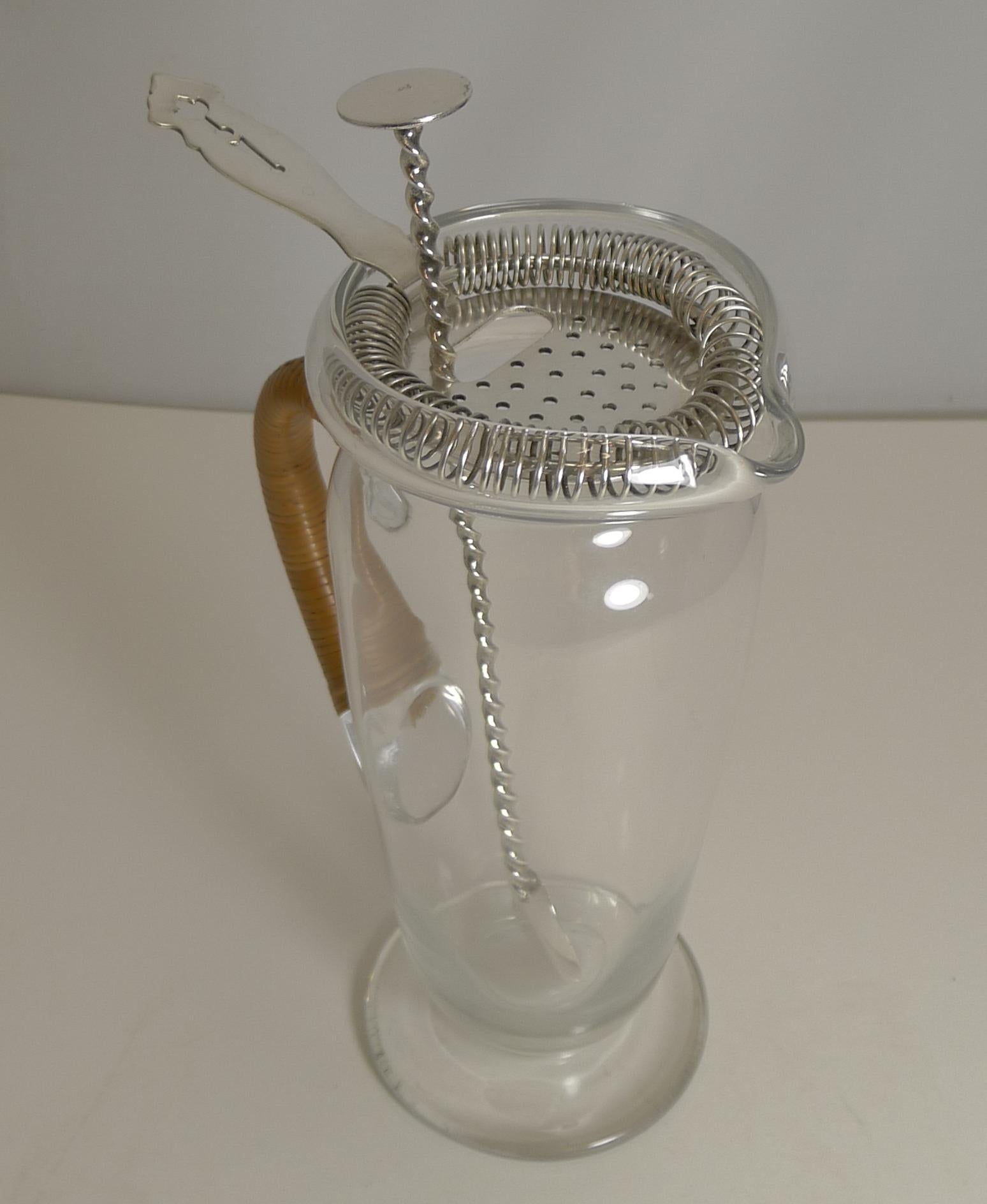 A smart 1930s glass and silver plated Martini / Cocktail mixing jug or pitcher with a cane wrapped handle.

The jug comes complete with the original strainer and mixing spoon. The strainer is signed by the creme de la creme of silversmith's,