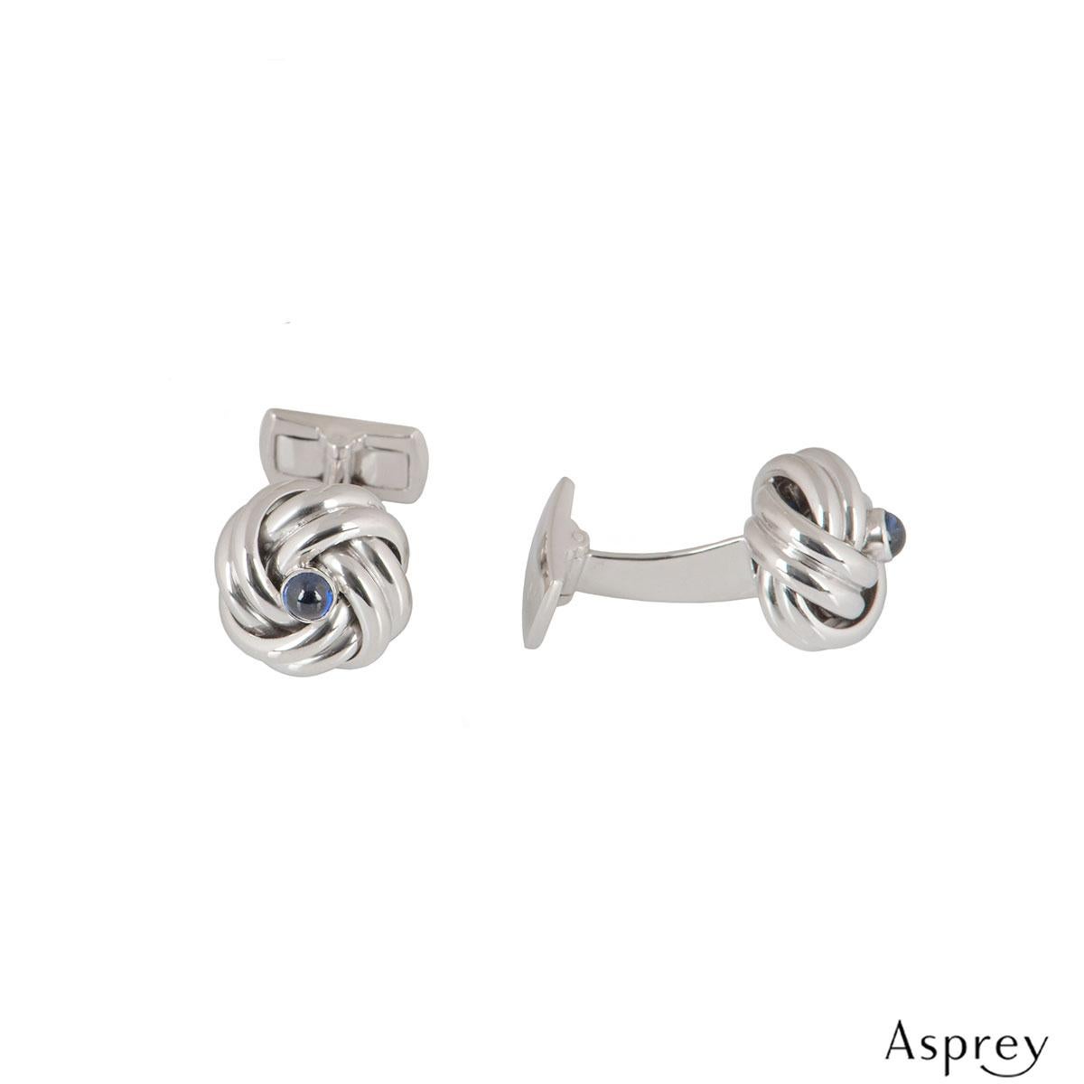 An 18k white gold pair of Asprey cufflinks. The cufflinks have a knot design set with a cabochon cut sapphire in the middle with an approximate total weight of 0.24ct. The cufflinks feature t-bar fittings with a length of 2.50cm. The knot measures