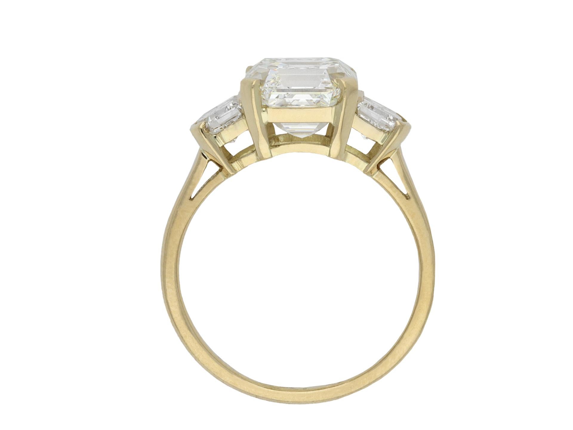 Asscher cut diamond flanked solitaire ring. Set with an Asscher diamond, H colour, VVS1 clarity, with an approximate weight of 3.03 carats in an open back claw setting, further set with two D-shape step cut diamonds in open back half rubover