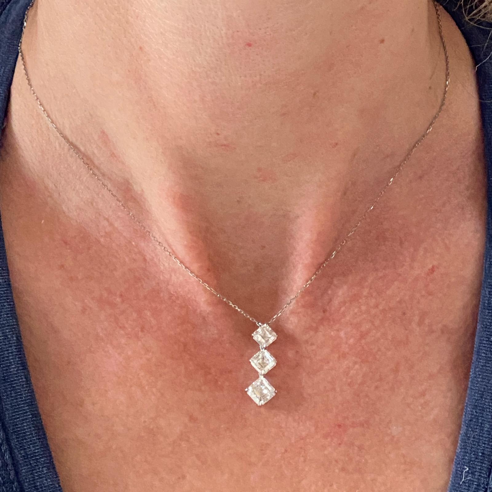 Three stone drop pendant necklace fashioned in platinum. Three high quality asscher cut diamonds drop 1 inch and feature all GIA certified diamonds. The largest diamond weighs .94 carats and is graded G/VS1, the .77 carat diamond is graded G color