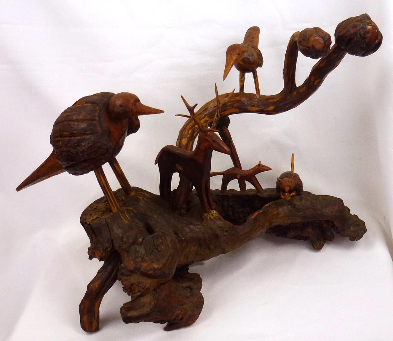 This is an assemblage of carved birds and animals by Russell Gillespie. The figures are carved from burls, branches, and wood, mounted on a larger root base. There are two birds, a deer with carved antlers, a squirrel with a nut, and another small