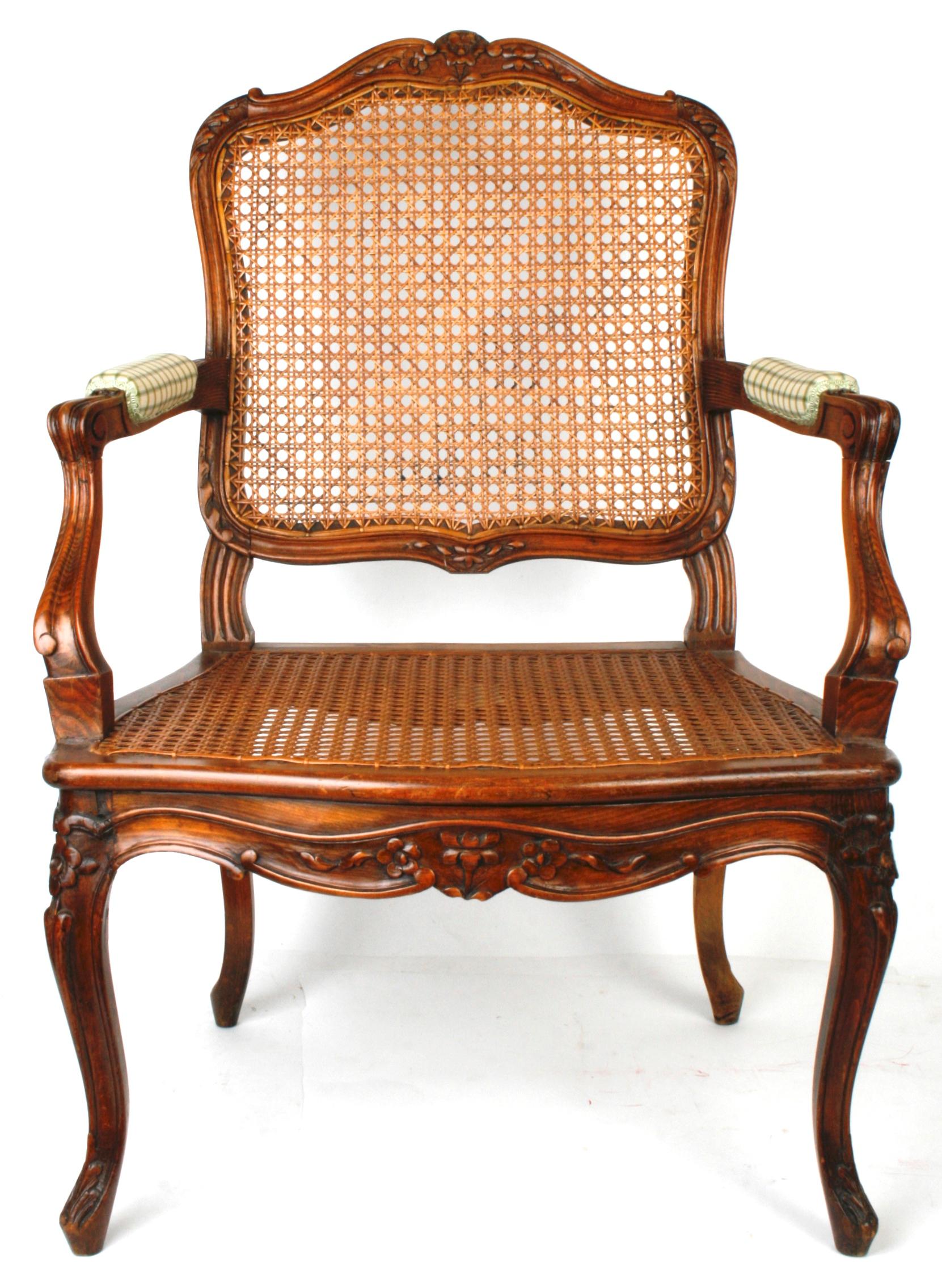 An assembled pair of Louis XV style French carved walnut dining chairs with hand-caned seats and backs with upholstered arms. The frames are constructed in the 18th century Louis XV manner with pinned mortise and tenons and have a scrolled floral