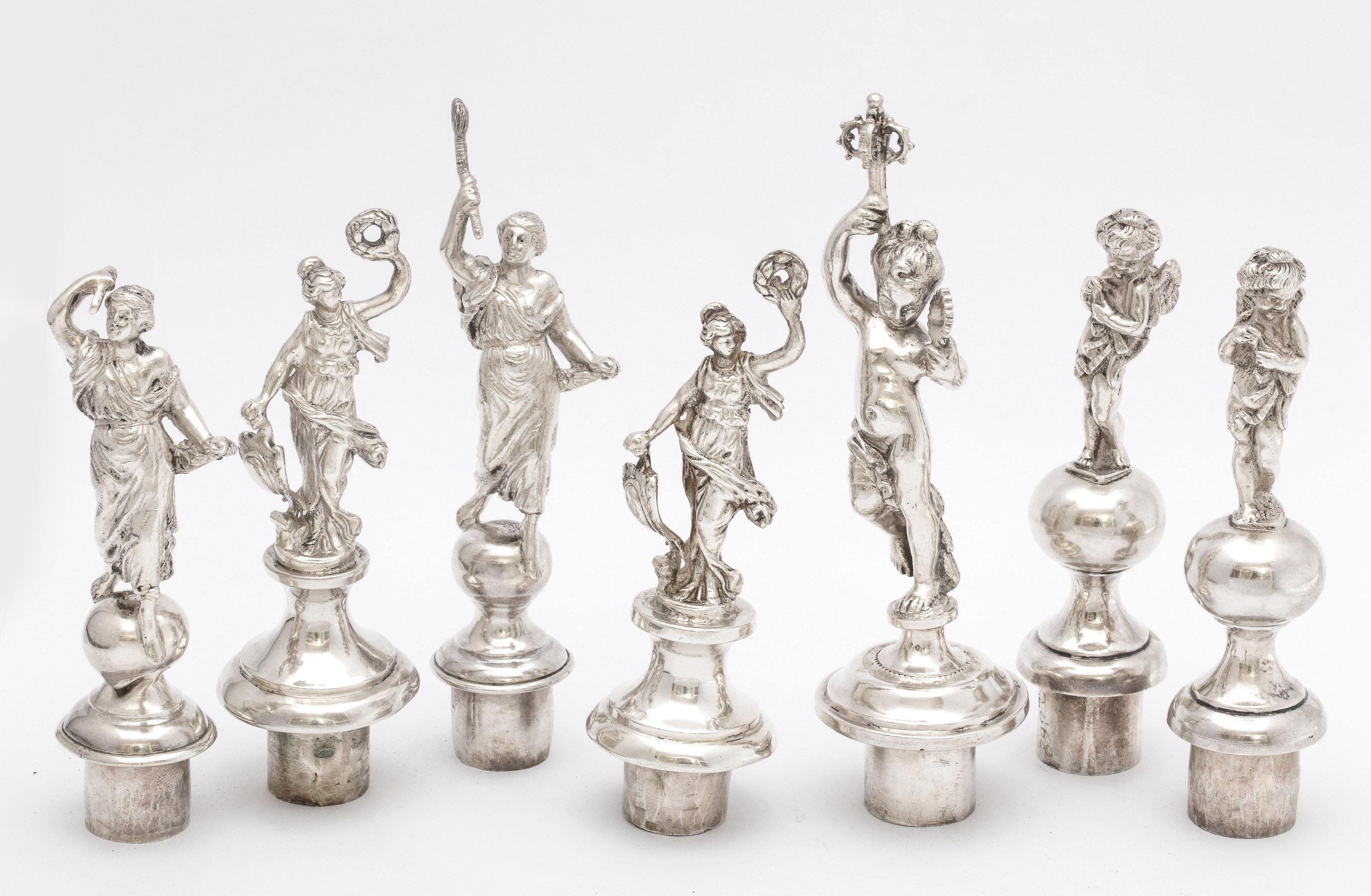 Unusual, Victorian period, assembled set of continental silver (.800) neoclassical, figural wine bottle stoppers, European, circa 1880s.The set consist of seven (7) stoppers and the wooden base. Each stopper has an opening in the bottom in which to