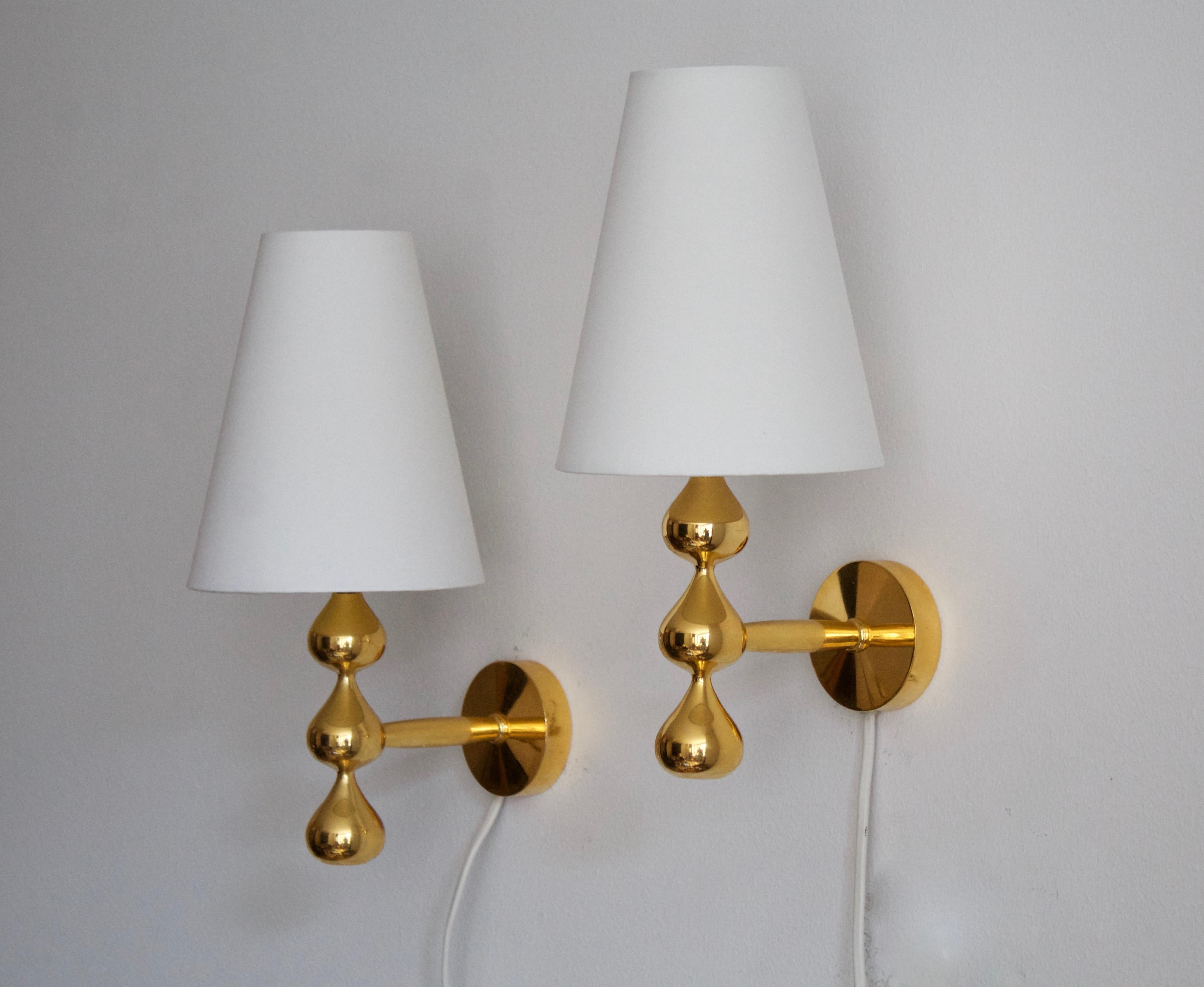 A pair of wall lights / sconces. Designed and produced by Assmussen Design, Denmark, firm founded in 1975, this pair of sconces produced c. 1980s. 

In 24-karat gold plate. Brand new lampshades.