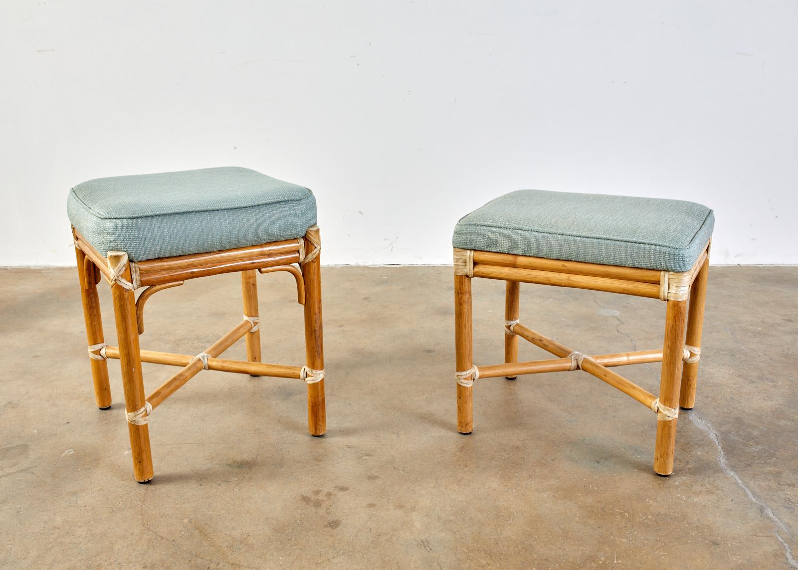 Near match associated pair of McGuire bamboo rattan stools or footstools. Made in the organic modern style crafted from rattan with leather rawhide laces on the exposed joints. The thick cushion tops are upholstered with a celadon colored fabric and