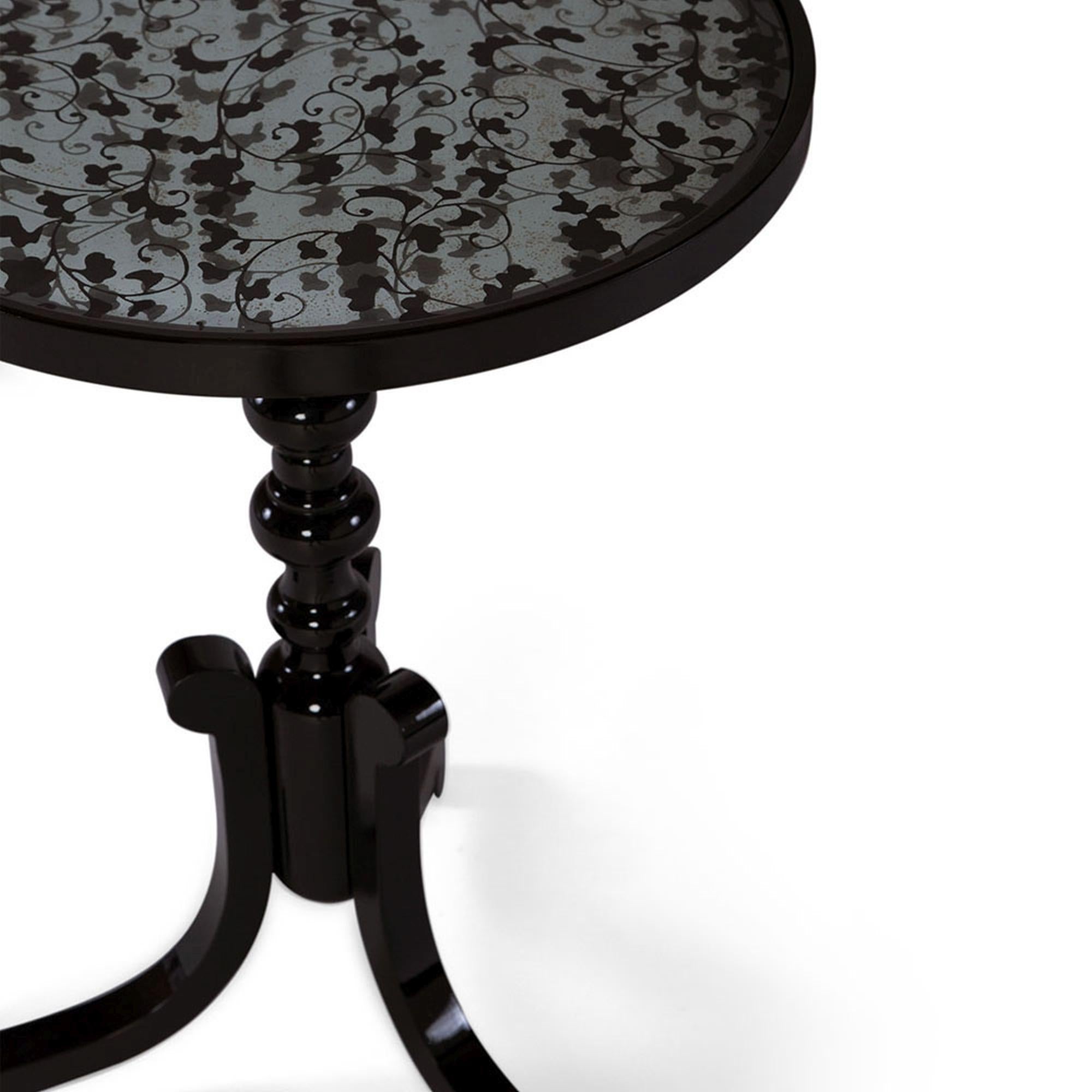 The Astaire accent table I is a delicately ornate and exquisite piece. This accent table includes a recessed antiqued mirror with an inset hand embellished black floral design on tempered glass. The turned leg is carved by hand. Due to the