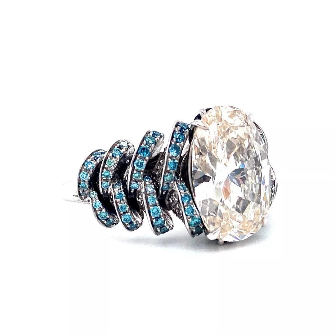 This 18K white gold “Estate” ring is from our Merveilles des Océans Collection. This unique ring has a certified oval cut 5.57 Carat white diamond in J color and VVS1 clarity decorated with 120 blue diamonds in total of 0.65 Carat, 178 white