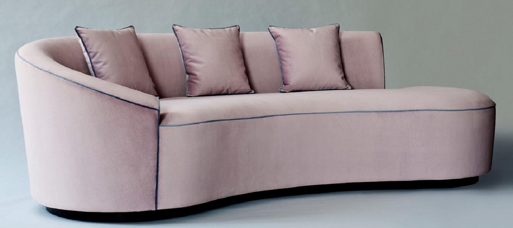 A discreet oak base anchors the serpentine upholstery of the Astra Sofa, available with or without contrast piping. Its single arm (either left or right-facing) curves to become the low back that runs part way along the seat, elegantly cradling a