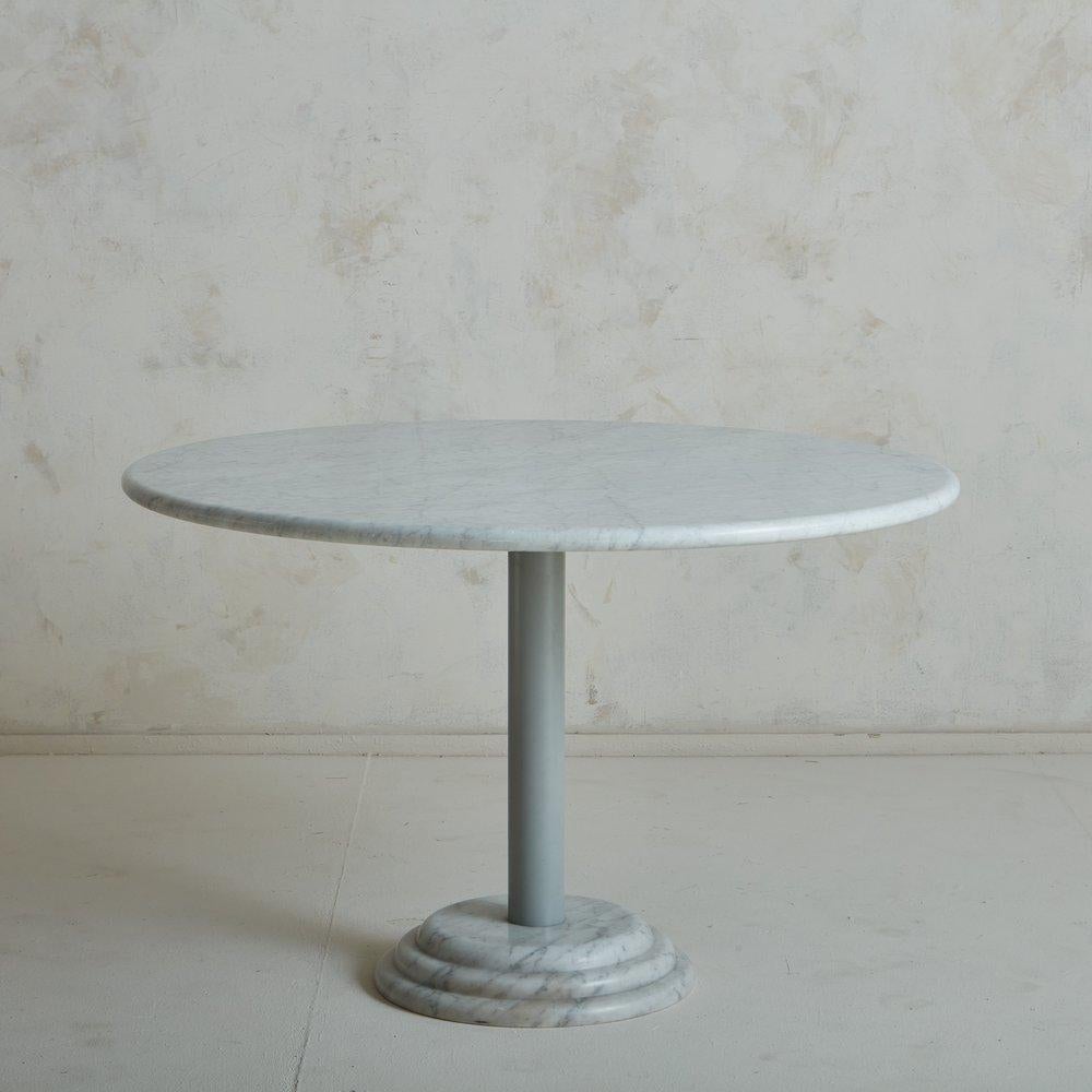A 1980s Italian ‘Astragalo’ pedestal base dining table by Antonia Astoria. This table has a 1.25” thick round Carrara marble tabletop with gorgeous gray veining and an elegant bullnose edge. It has a tubular gray metal center column, which is