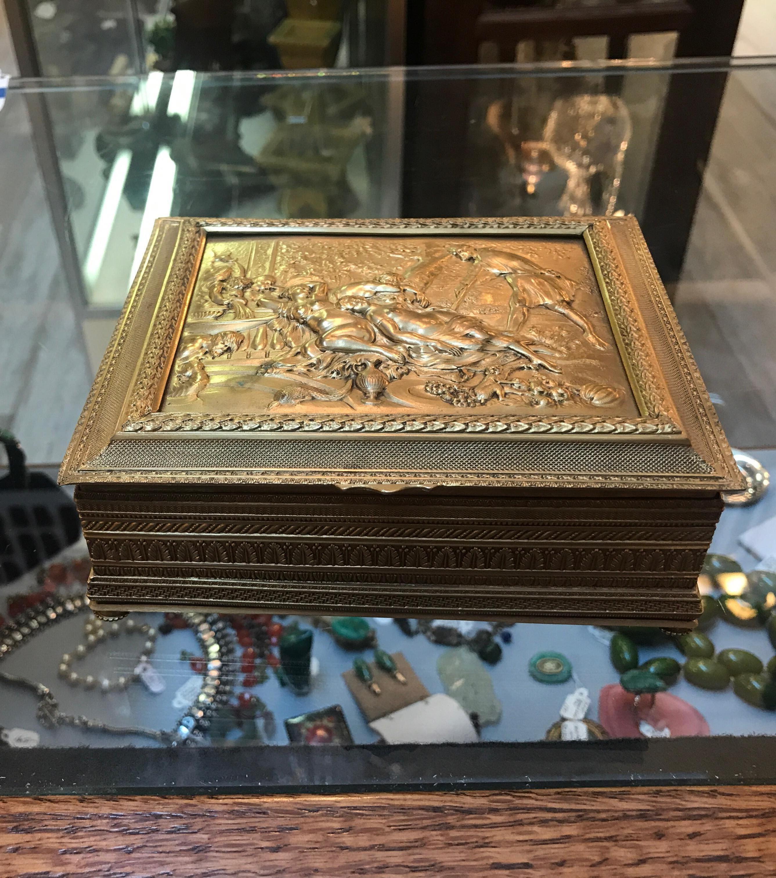 Schöne Tischdose aus vergoldeter Bronze, Österreich, um 1900. Die allegorische Szene mit gedrechselten Details am Rand und an den Seiten ruht auf vier kleinen Bronzeknopffüßen. Linie aus bestickter Seide.