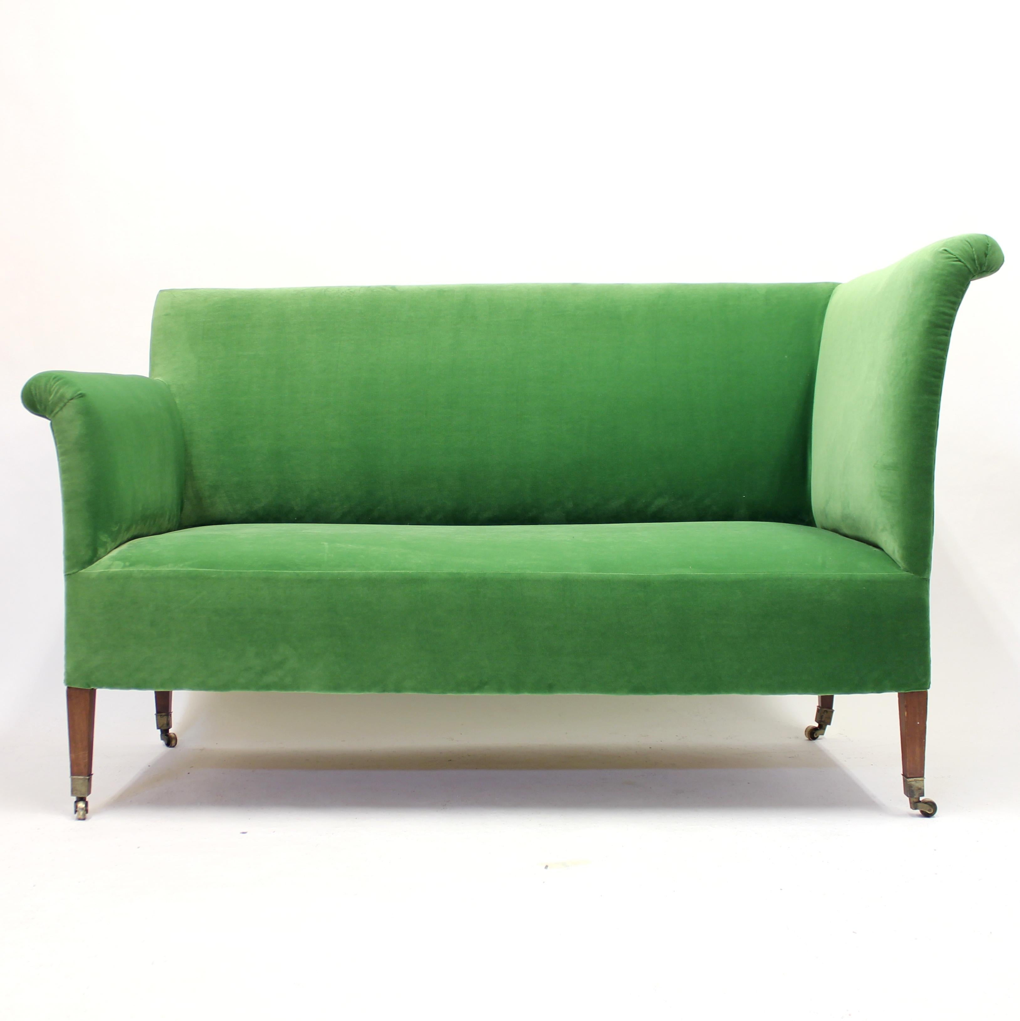 Rare asymmetric sofa with brass castors on mahogany legs from the early 20th century. The two armrests are totally different in height which creates a very unusual and eclectic shape one seldom sees from this period. New grass green velvet