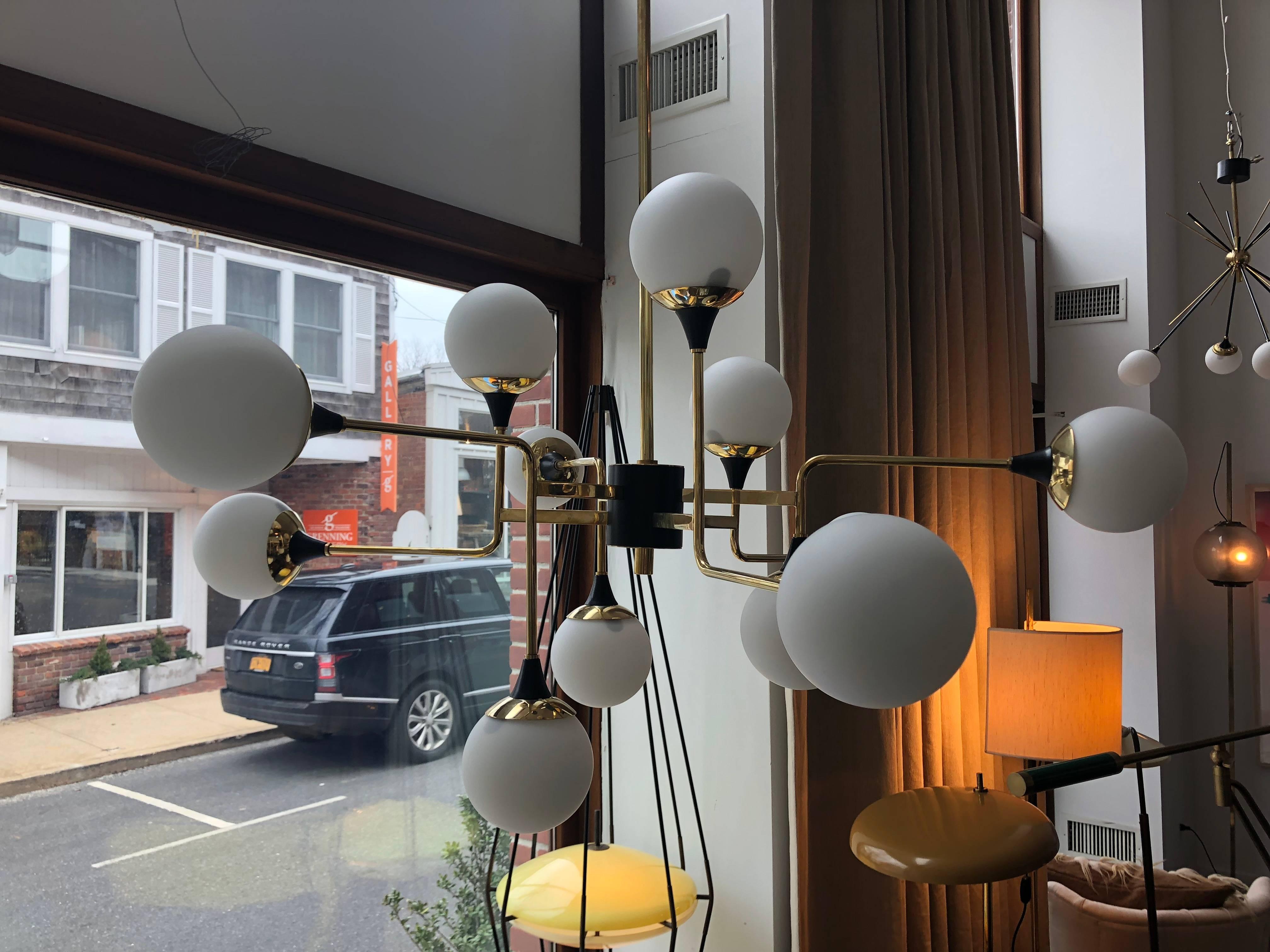 An asymmetric shaped chandelier composed by six bent brass arms with black enamel details in the style of Stilnovo midcentury. 12 hand blown white glass globes made in Italy.
 