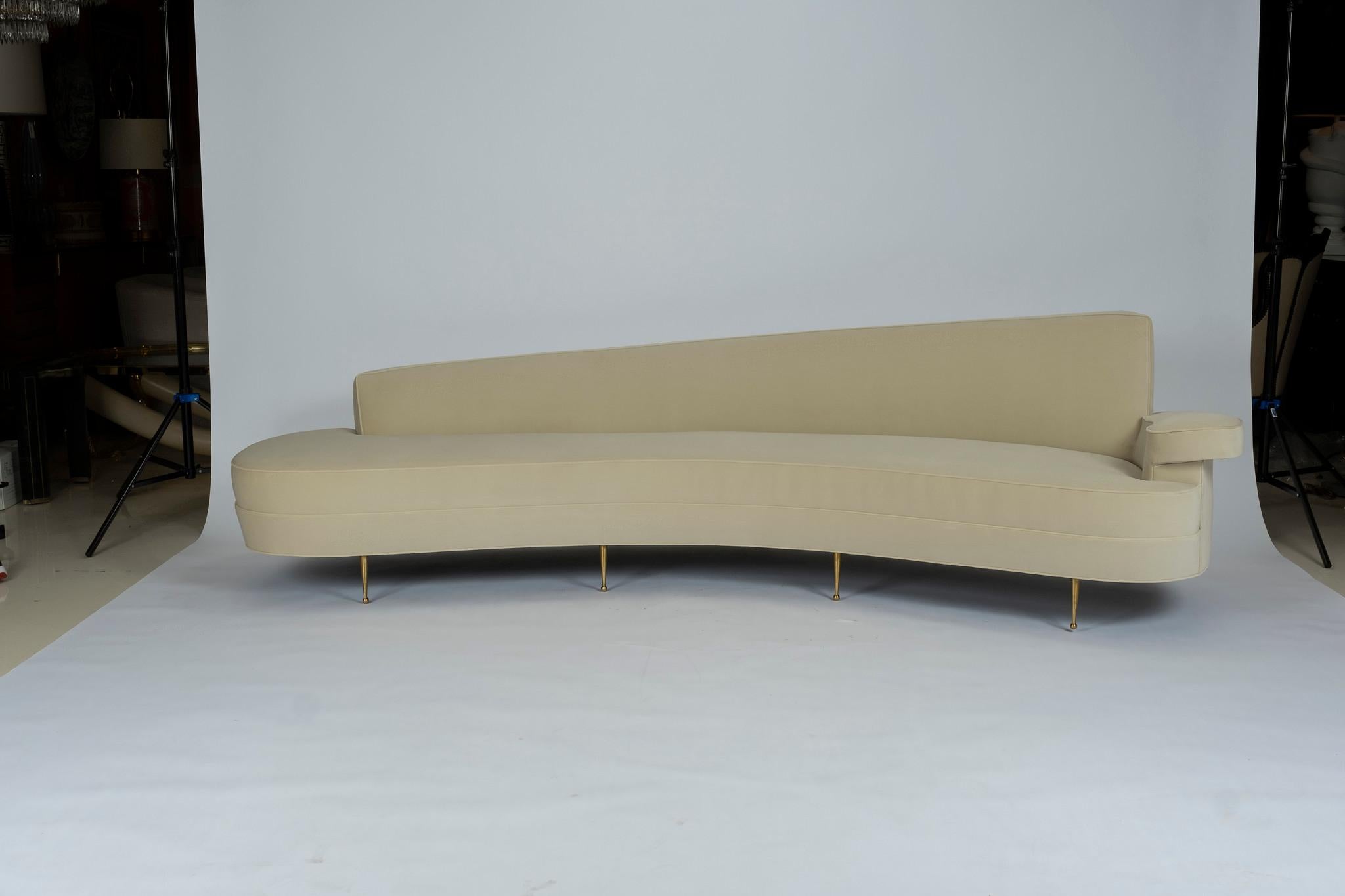 A magnificent asymmetrical curved back sofa upholstered in a creamy ecru velvet. This beautiful sofa is supported by solid brass sabots. We stripped the original 1950s Federico Munari Italian sofa down to its frame and copied it to exact