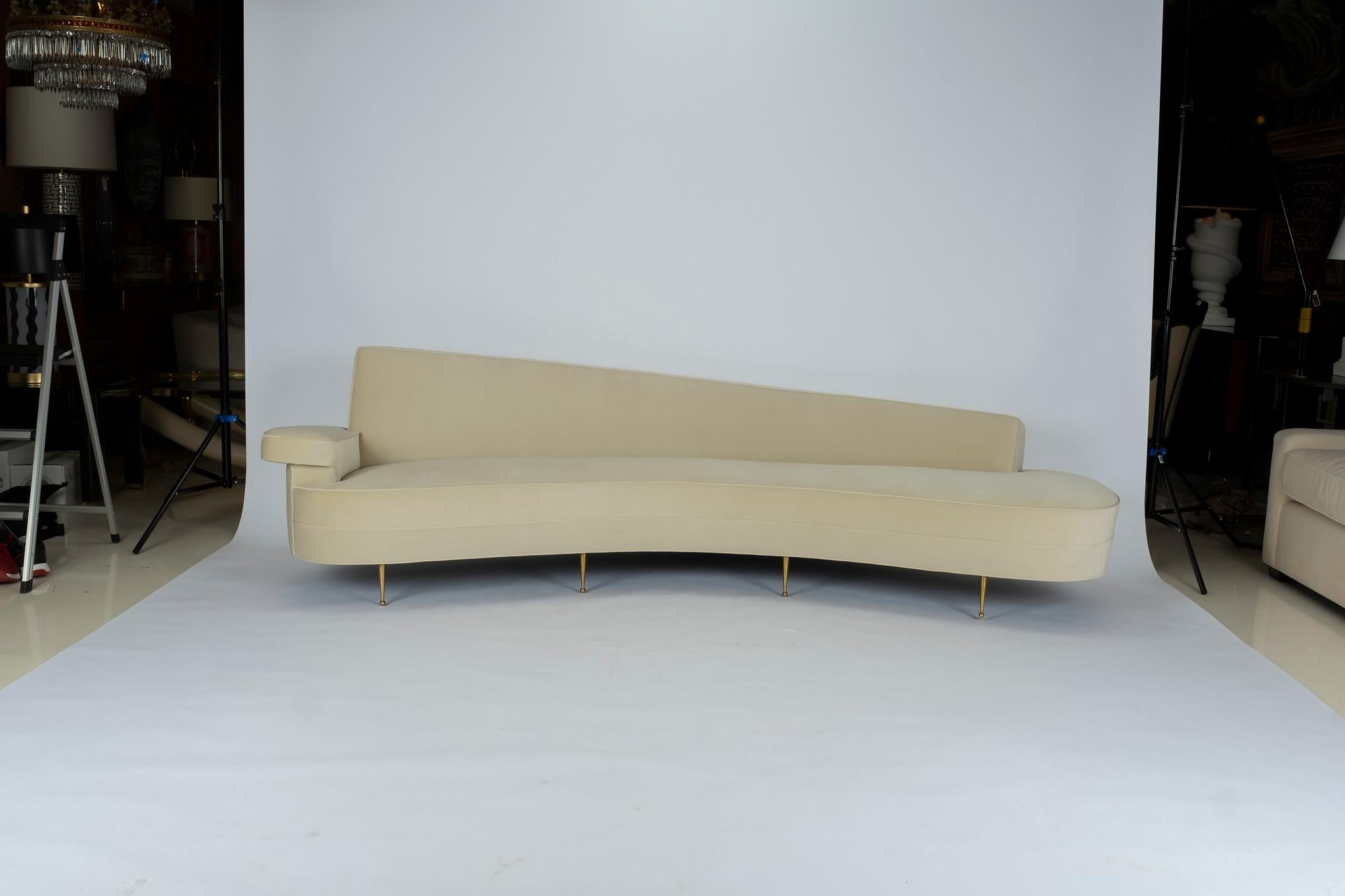 A magnificent asymmetrical right arm curved back sofa upholstered in a creamy ecru velvet. This beautiful sofa is supported by solid brass sabots. We stripped the original 1950s Federico Munari Italian sofa down to its frame and copied it to exact