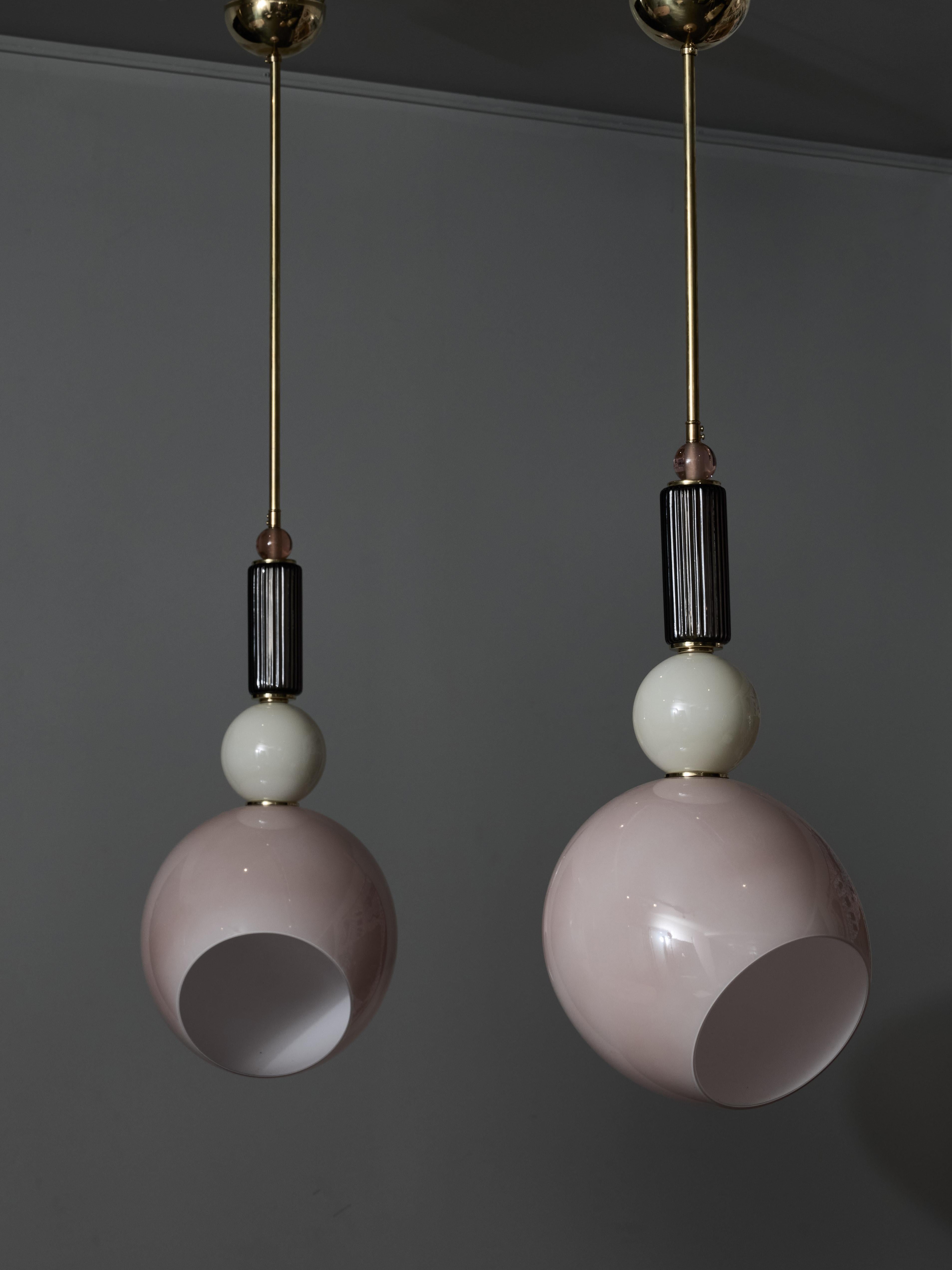 Ciondoli realizzati con pezzi di vetro di Murano impilati ed elementi in ottone, conclusi da un grande globo rosa asimmetrico a forma di ovoide che contiene una sorgente luminosa.