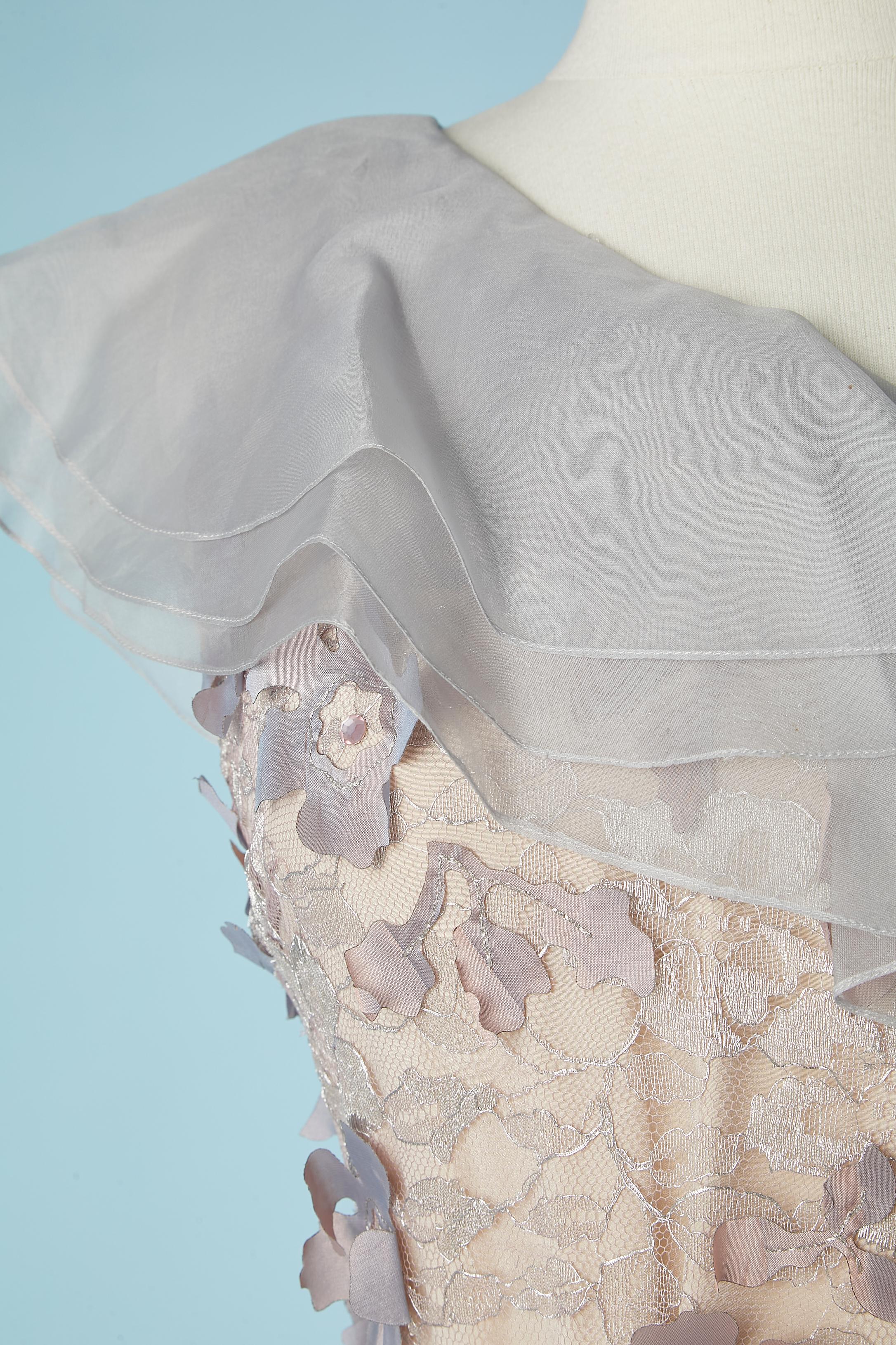 Asymmetrisches pastellfarbenes Abendkleid mit Blumenapplikation mit Strass auf silberner Lurexspitze. Organza-Rüschen am Halsausschnitt. Unsichtbarer Reißverschluss und Haken&Öse auf der linken Seite.Stoffzusammensetzung: 47% Polyamid, 41% Viskose,