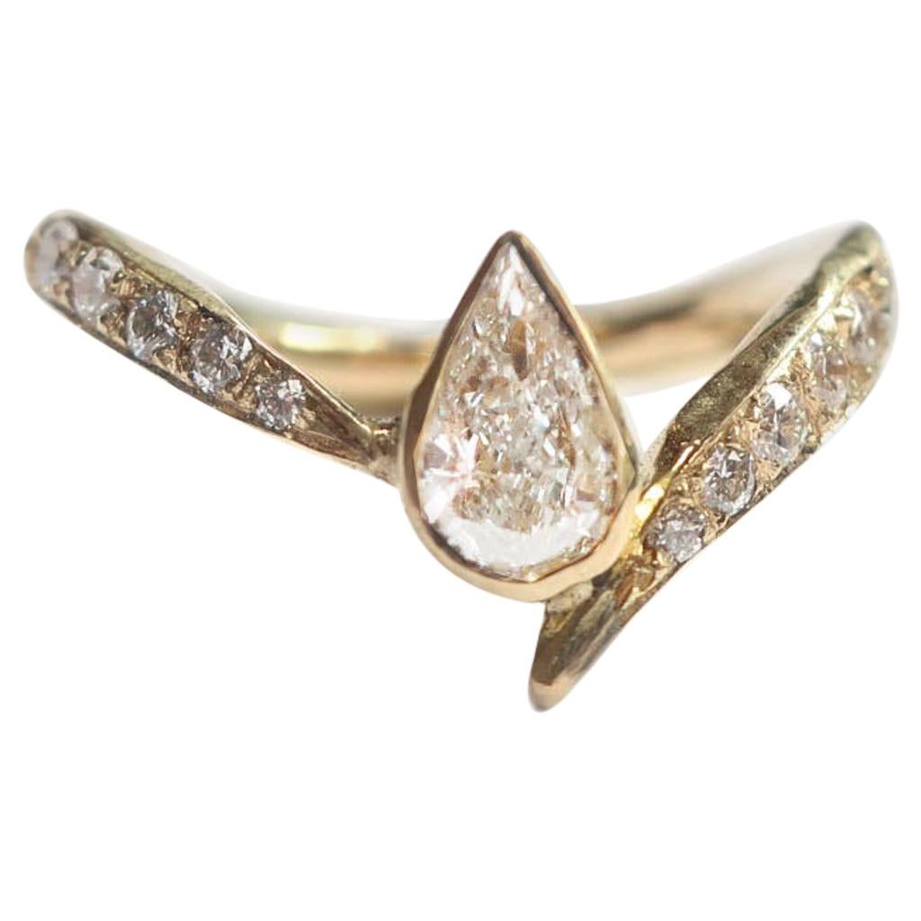 This is a bold alternative to the typical engagement ring. A hand carved asymmetrical band wraps around the finger set with vs white diamonds. A stunning pear cut white diamond is bezel set in 18k gold nestled nicely in the cradle of the band. This