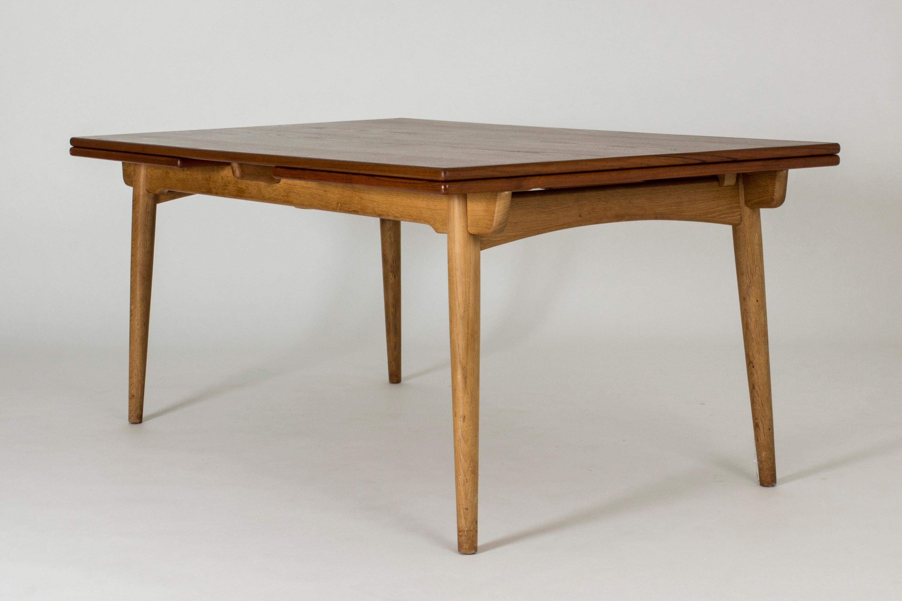 Large and versatile dining table by Hans J. Wegner, with teak top and oak legs. Two extra leaves measuring 60 cm each are cleverly hidden inside the table and are easily extended. The table looks great both with and without the extra leaves.