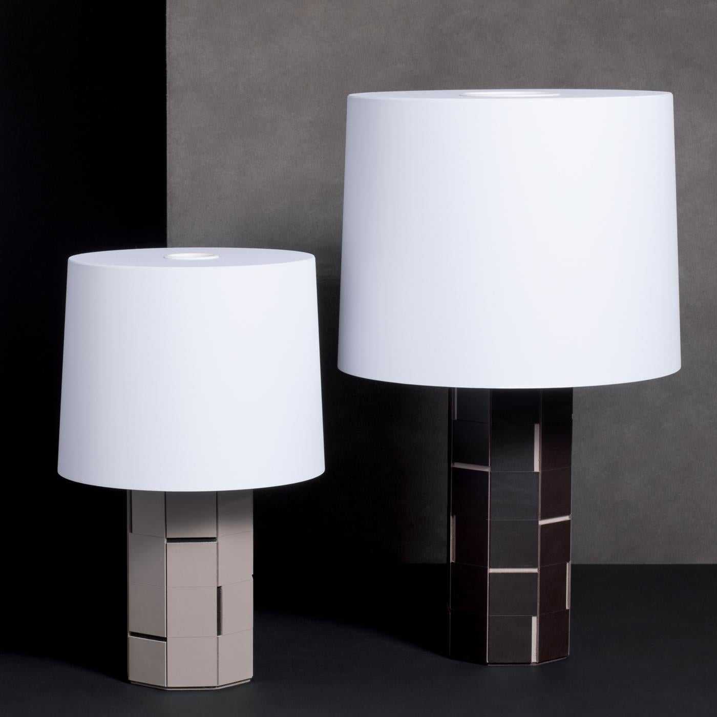 This unique table lamp, part of the Atari collection, will look right at home with any style. It features a base made of saddle leather white tiles with black grooves and a white shade that diffuses a soft light. The overall effect is of textural