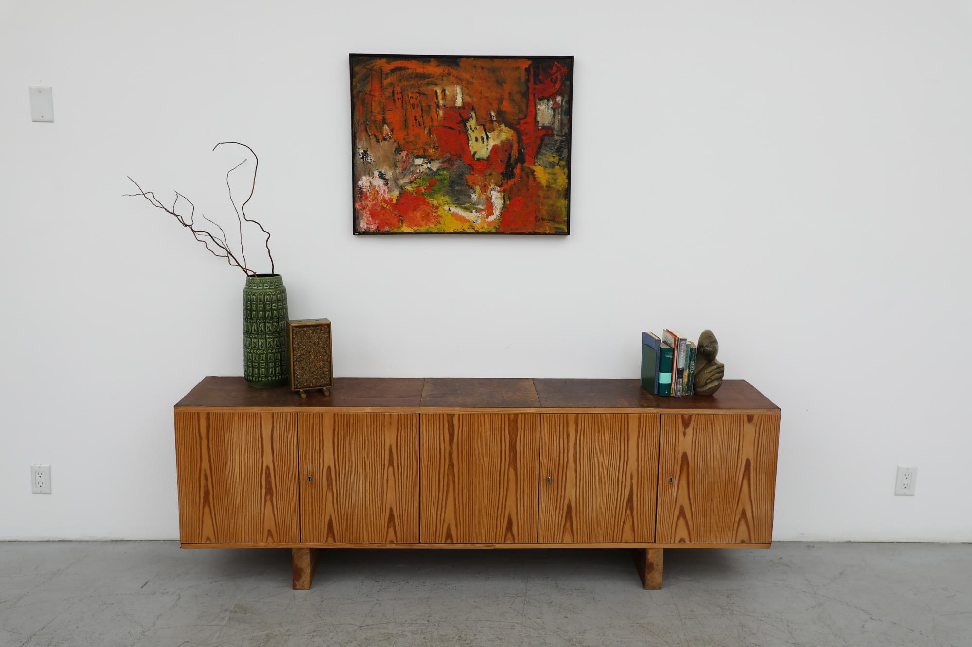 Ate Van Apeldoorn inspired long pine credenza with leather top and sides, and vibrant vertical stripe grain. Each door locks using the same key. In original condition with visible wear consistent with its age and use. The leather addition is not
