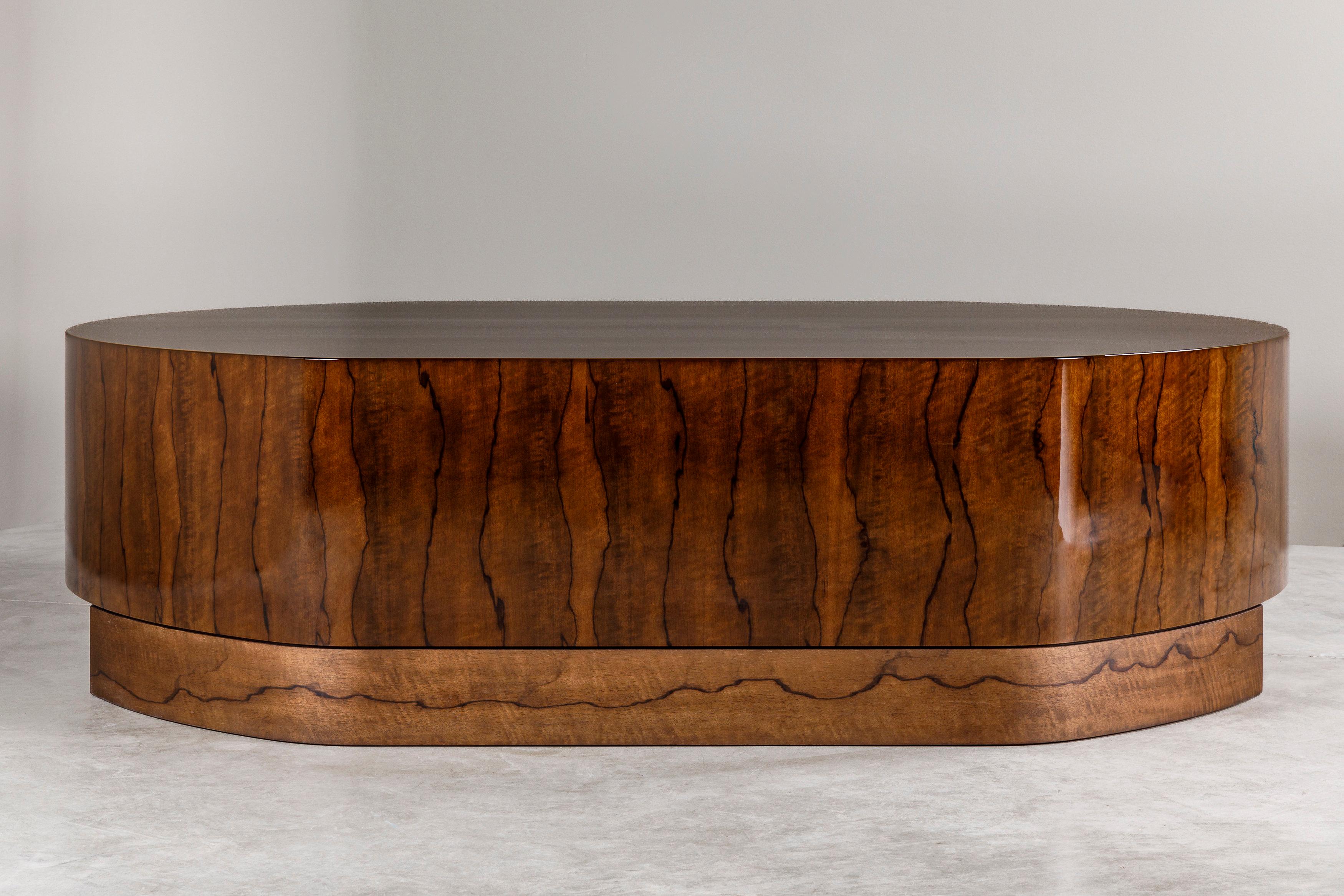 The ECU coffee table, created in 2023 by Atelier Linné, is made from an African wood called Limba Superba, recognizable by its dark veins on a blond background. The table has an oblong shape and rests on a recessed solid base. The alternating use of