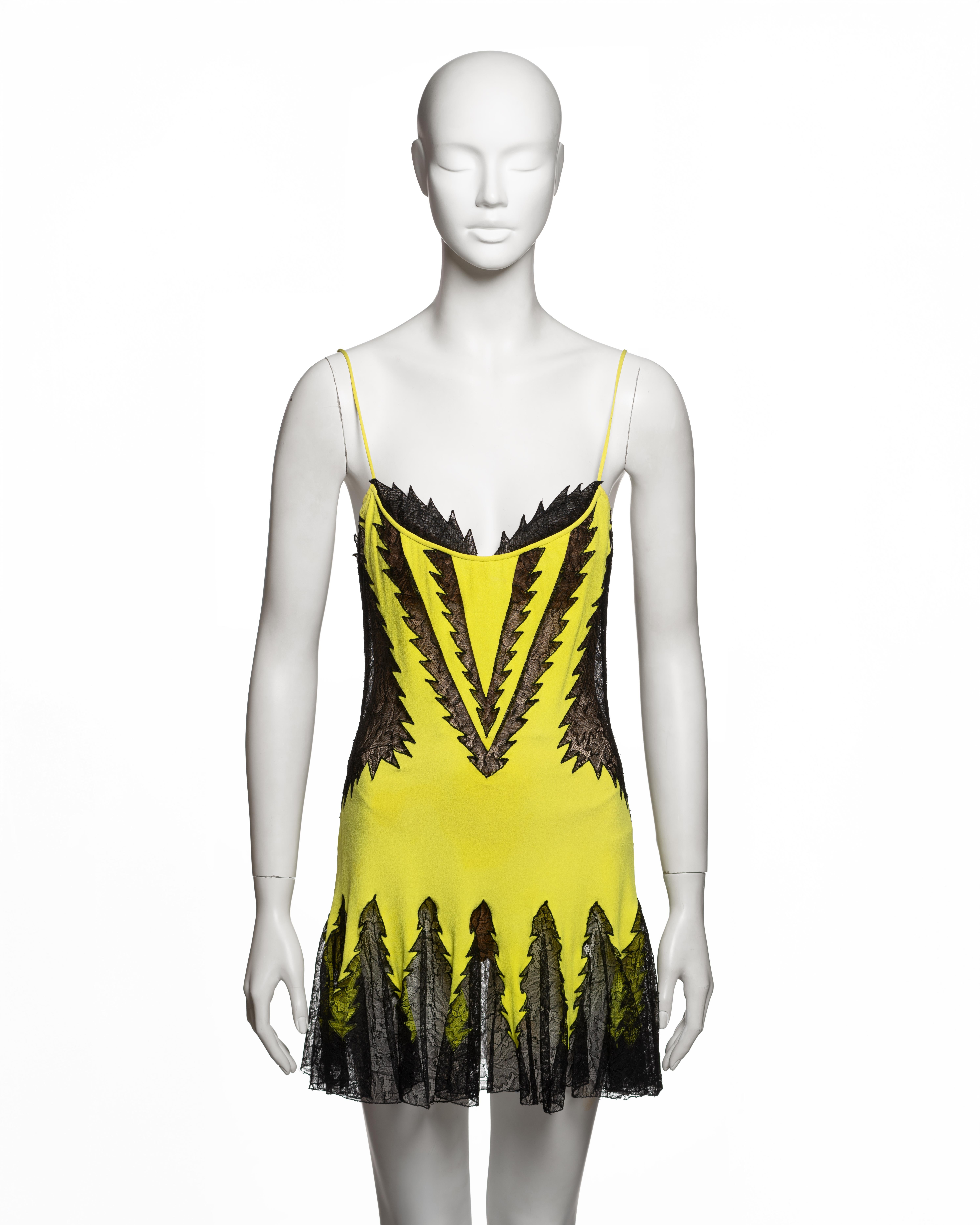 Minivestido de alta costura a medida Atelier Versace del año 2002,  confeccionada en crepé de seda color chartreuse con inserciones de encaje negro con motivos angulosos y llameantes que irradian desde el escote, la cintura y el bajo. La silueta
