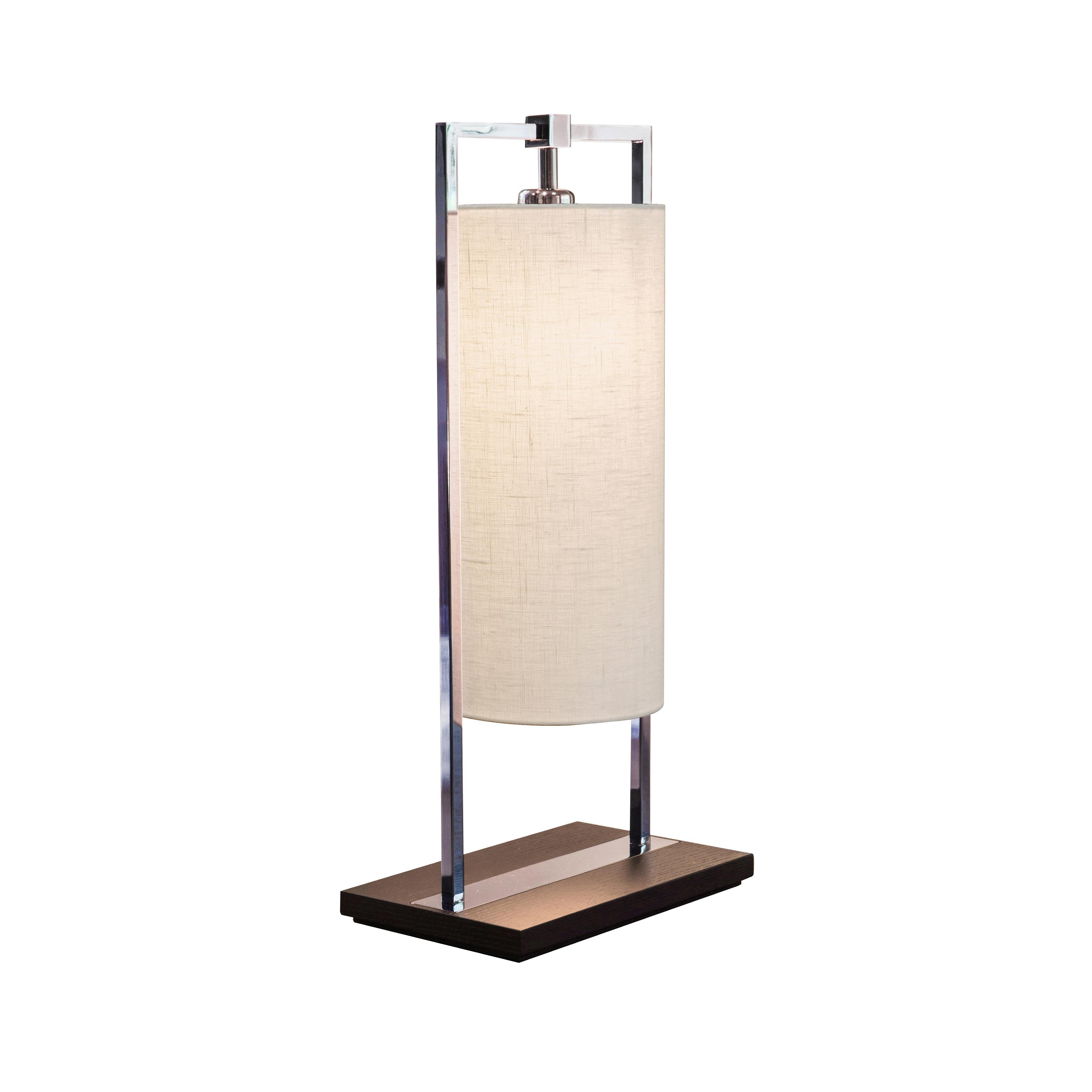 Athena is a table lamp characterised by rectangles (the base) and ovals (the shade) that blend together. The shade can be made with highly tactile fabrics, in linen or percaline, for a couture touch. The base is in dark brown stained oak with black
