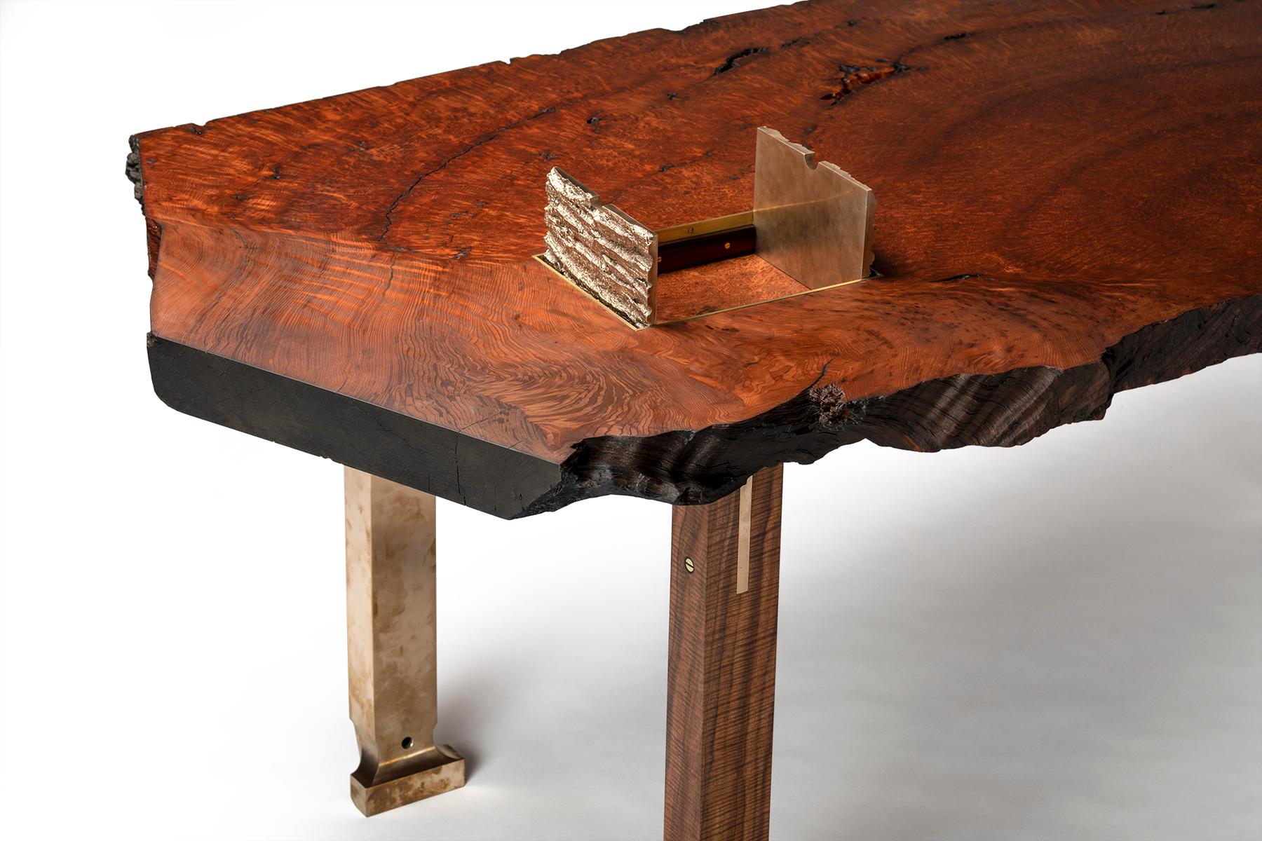 The Athol desk by Taylor Donsker features a live edge pommele old growth Redwood slab with recessed cast bronze tree bark doors opening to a concealed compartment. Three interlocking, solid, musical grade Oregon Walnut legs feature sculpted cast