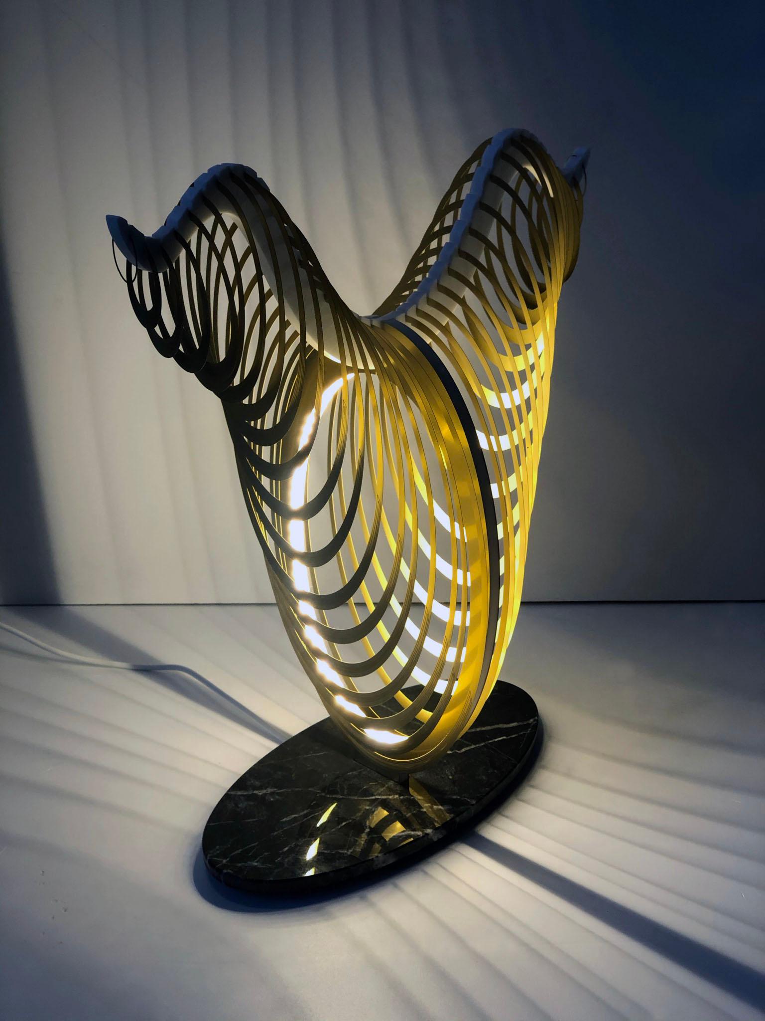 Symbolized by a cow and associated with motherhood, the Egyptian goddess Hathor inspired the unique design of this table lamp. The lamp features an elliptical brass element elegantly resting on a base of gray Carnico marble, creating a fascinating