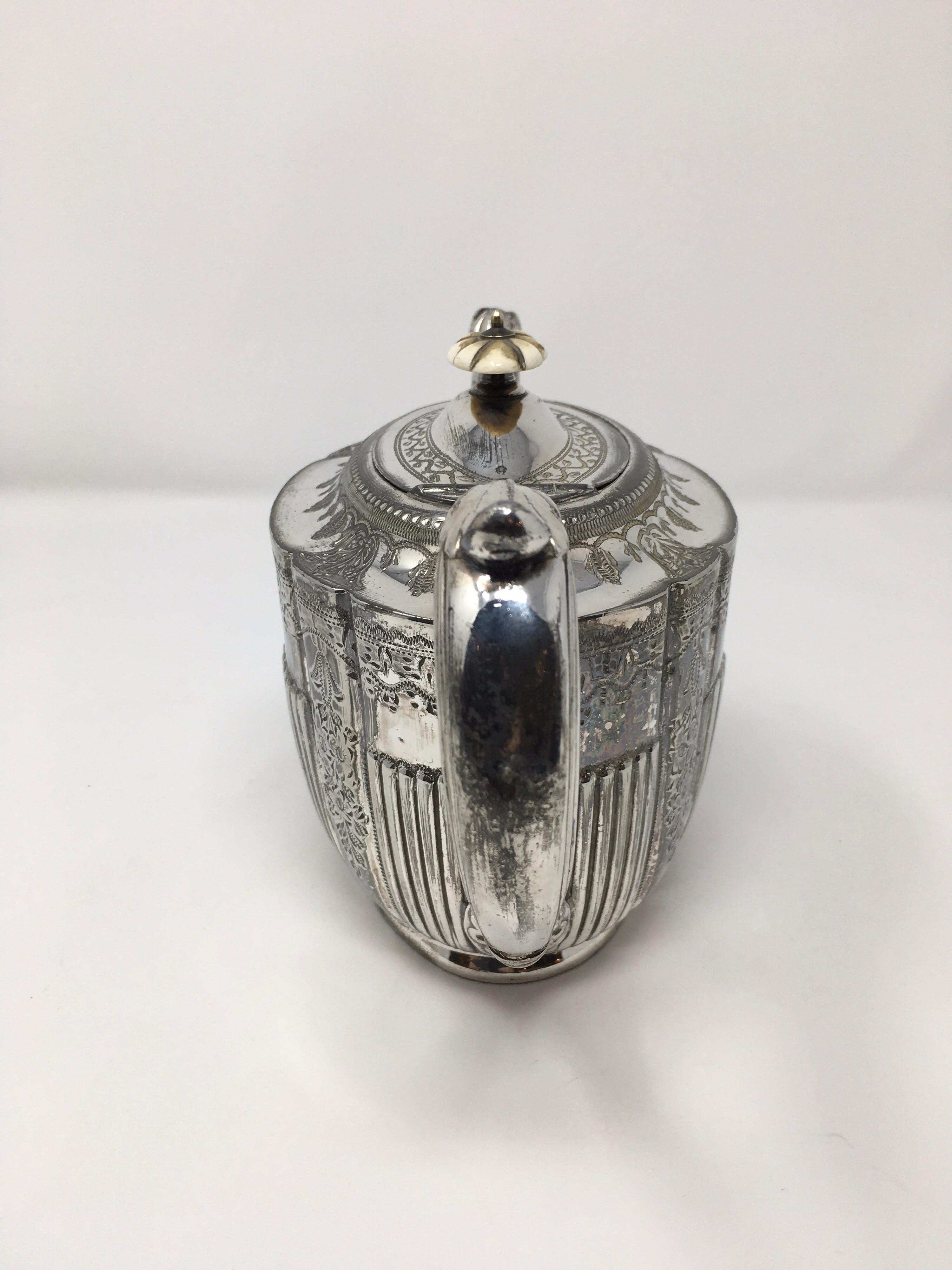 This is a lovely English silver plate teapot made by Atkin Brothers. The teapot has an attached lid and a lovely curved handle. The engraving on each side depicts floral and geometric shapes. The hall marks on the bottom of the piece lead us to