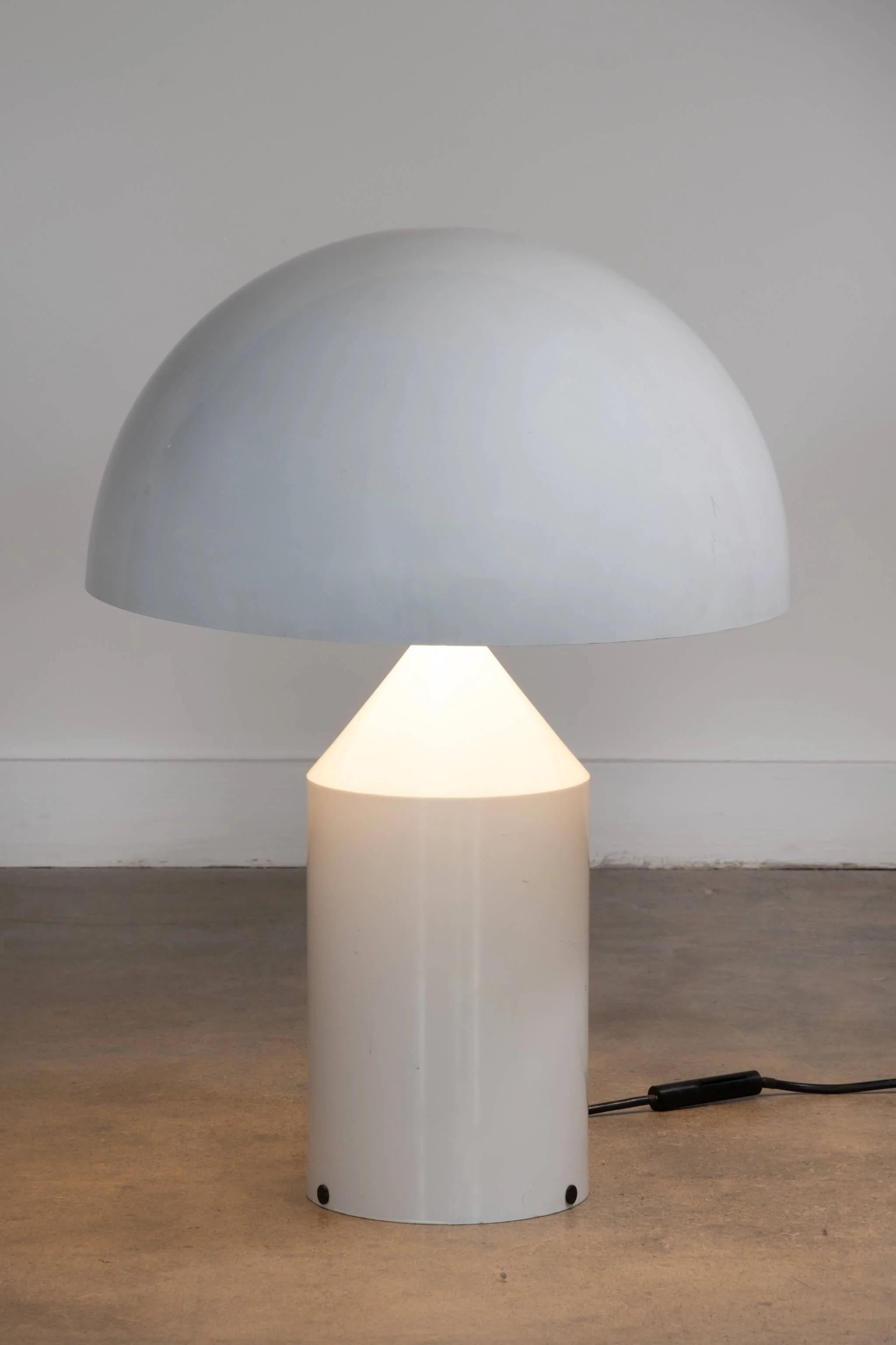 Icône du design italien de Vico Magistretti, la lampe à poser 'Atollo' est un produit à la fois décoratif et fonctionnel. Réalisée en aluminium peint, les formes géométriques qui la composent - cylindre, cône et hémisphère - sont une leçon