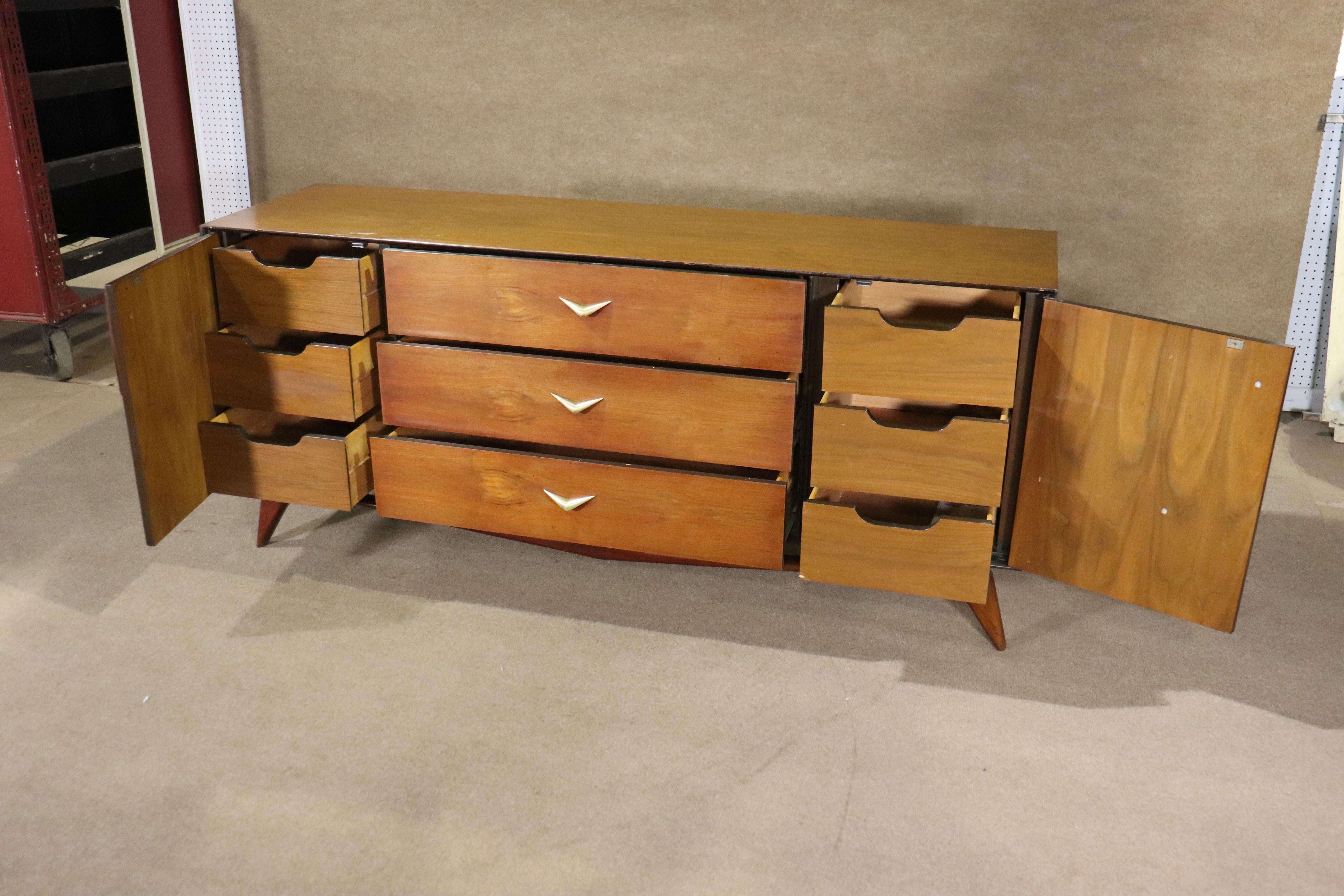 Mid-century modern nine drawer dresser in walnut wood grain and brass accent hardware. Beautifully sculpted wood base and matching boomerang handles. Dresser body seems to float above the wood base.
Please confirm location NY or NJ